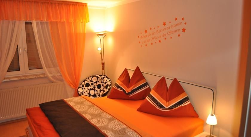 Gemütliches Schlafzimmer mit orangefarbener Bettwäsche und Vorhängen, dekorativen Kissen und Wandtattoo.