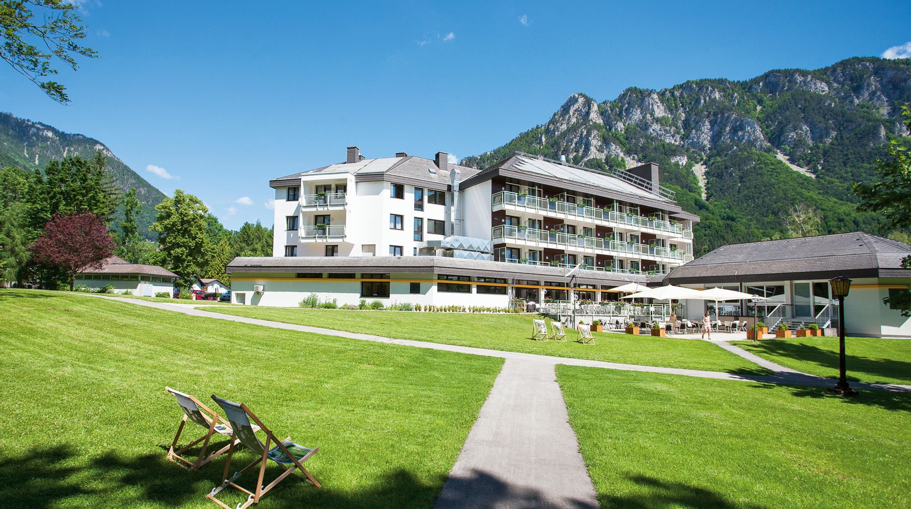 Parkhotel Hirschwang vor Bergkulisse mit grünem Rasen und Liegestühlen.