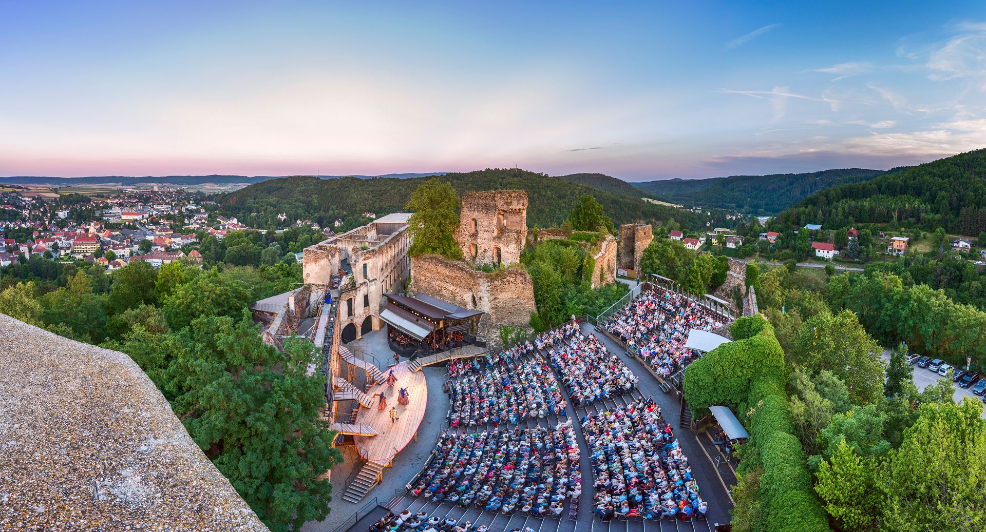 Panoramablick auf die Opernaufführung in der Burgruine Gars mit Publikum und umliegender Landschaft.