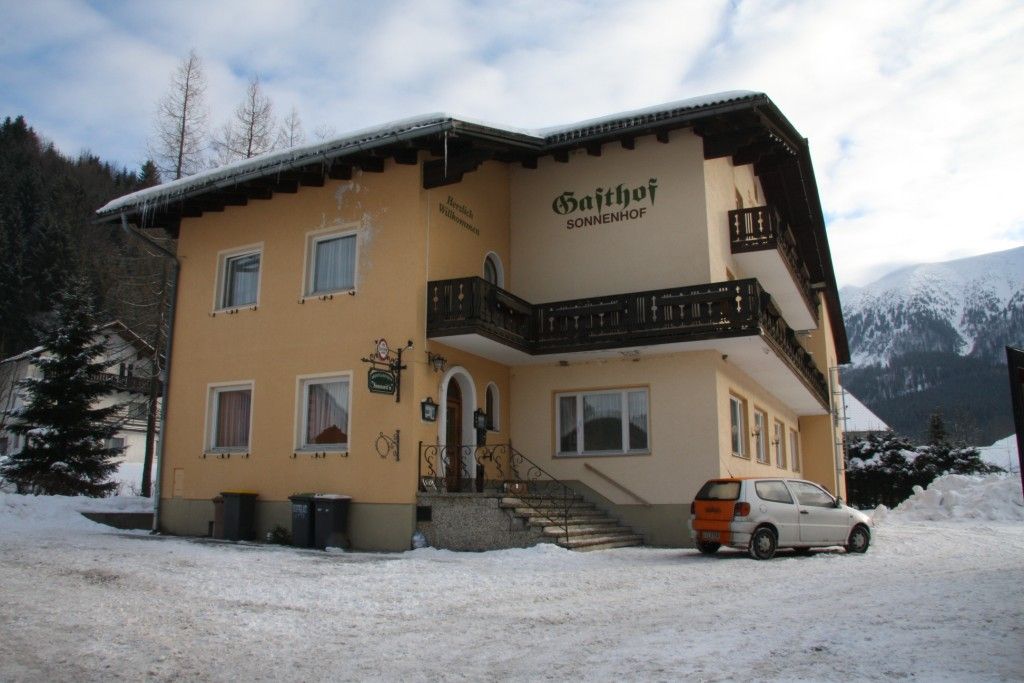 Ein gelbes Gebäude mit der Aufschrift 'Gasthof Sonnenhof' im Schnee, umgeben von Bergen.