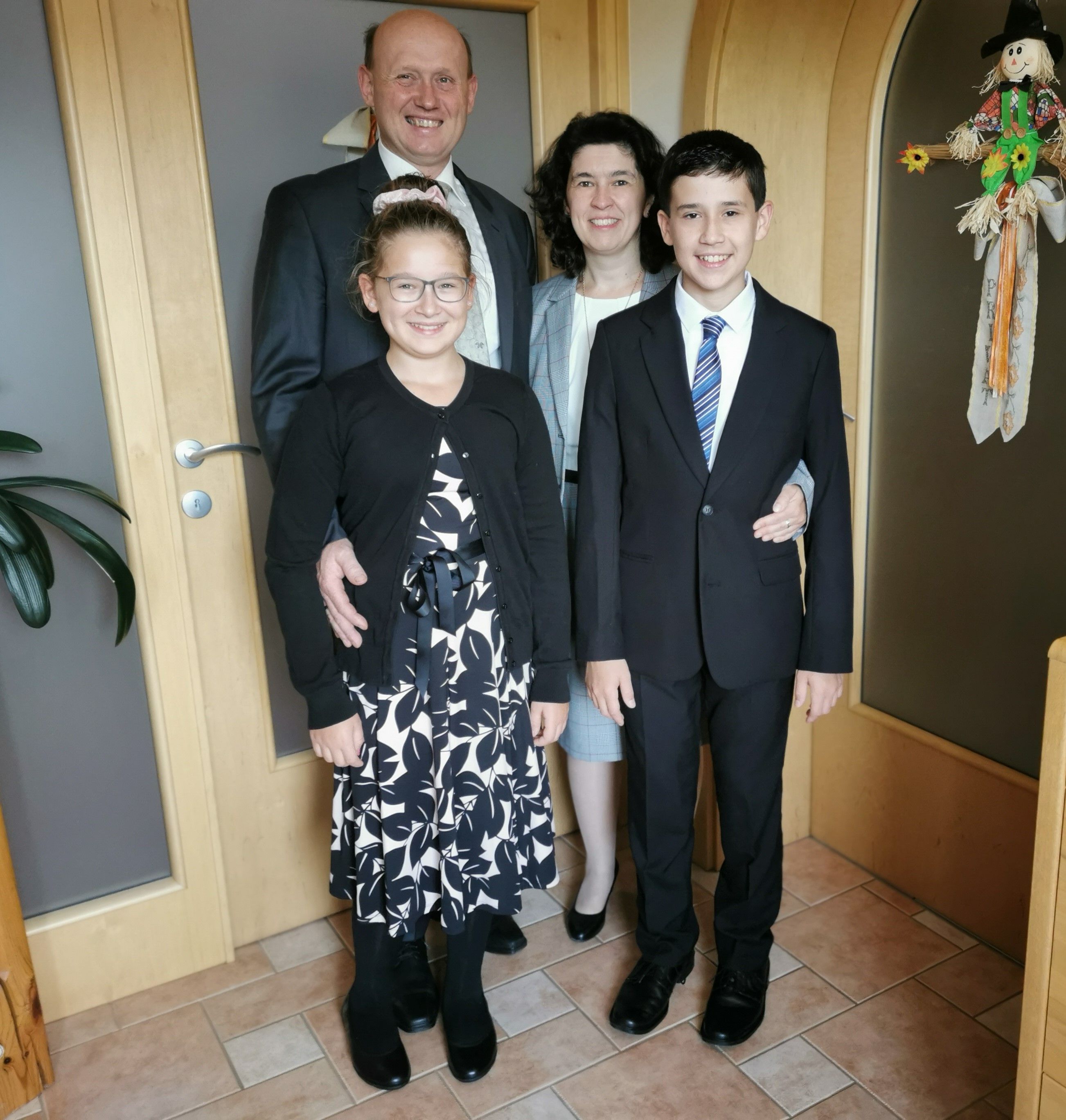Eine Familie in formeller Kleidung steht lächelnd in einem Flur.