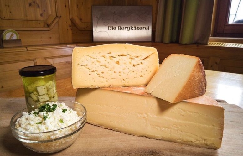 Verschiedene Käsesorten auf einem Holzbrett mit einem Glas eingelegtem Käse und einer Schüssel Frischkäse.
