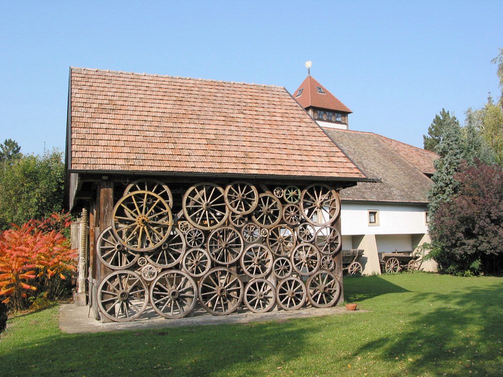 Ein Gebäude mit einer Fassade aus alten Wagenrädern, umgeben von Bäumen und einem Rasen.