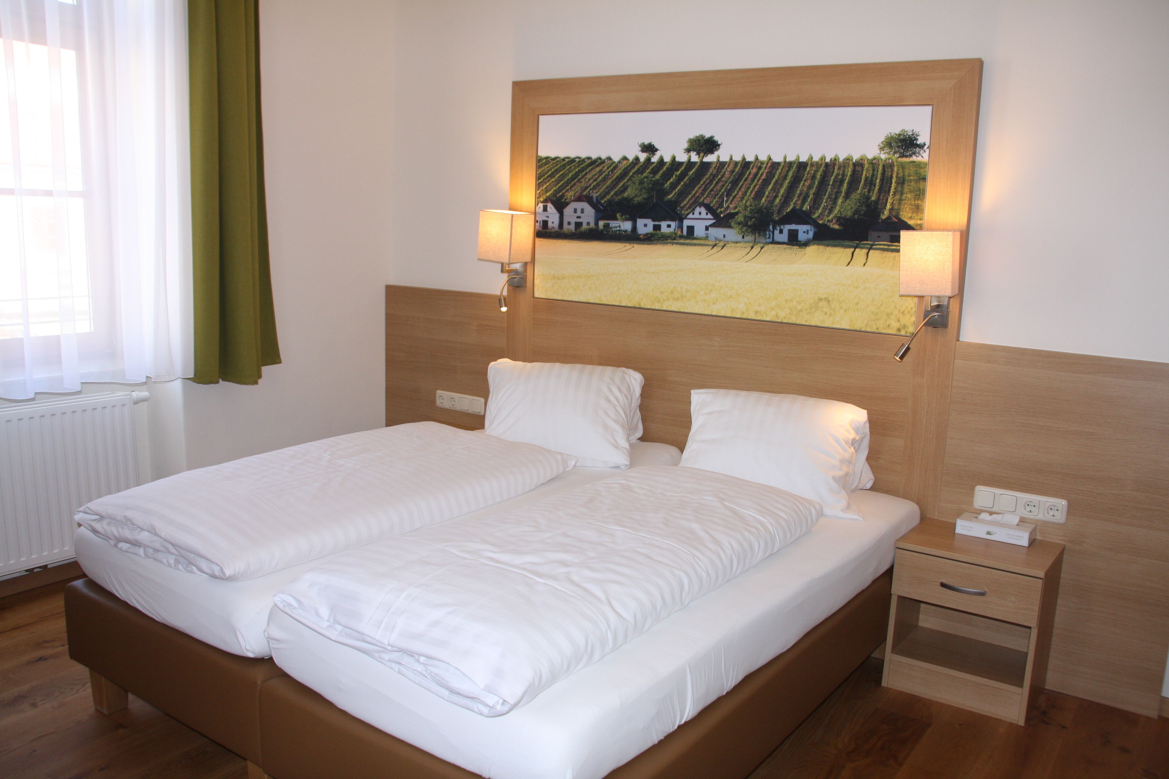 Ein Gästezimmer mit einem Doppelbett, Holzverkleidung, Nachttisch und einem Bild von Weinbergen an der Wand.