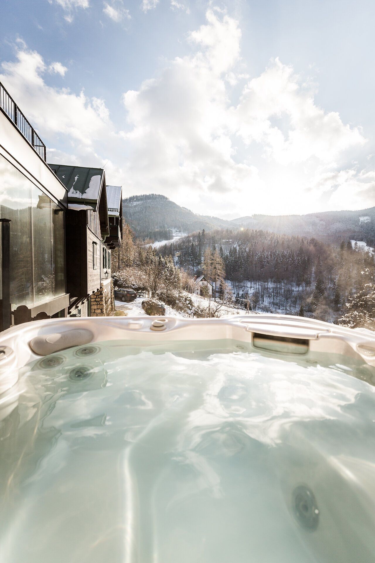 Zwei Personen stehen auf einer Terrasse mit Blick auf bewaldete Berge bei Sonnenuntergang.