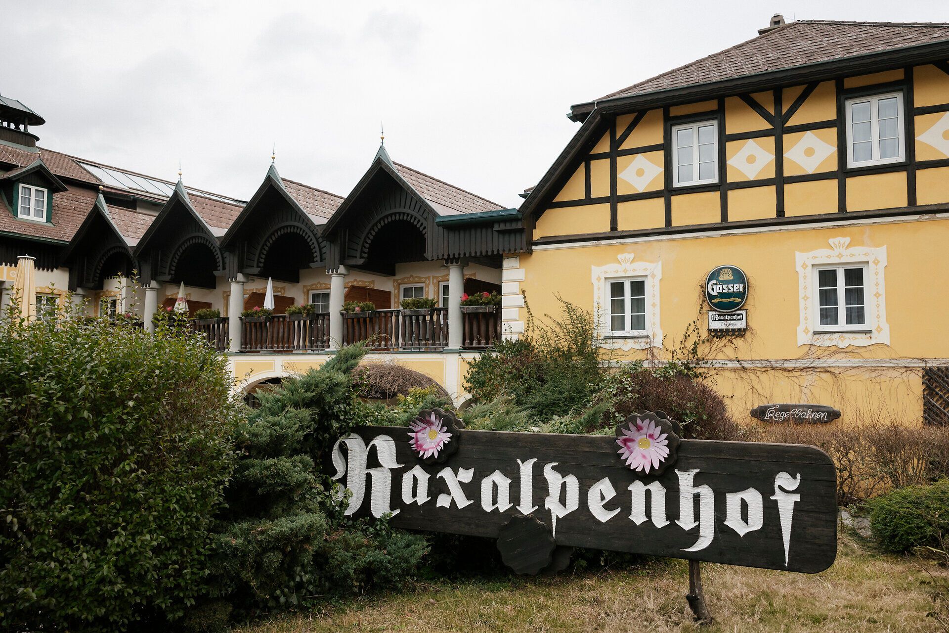 Traditionelles Gasthaus mit gelber Fassade und Holzveranden, davor ein Schild mit der Aufschrift „Raxalpenhof“.
