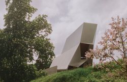 Der Wolkenturm in Grafenegg – moderne Freiluftbühne aus Beton und Stahl, umgeben von blühenden Bäumen und grüner Landschaft unter einem leicht bewölkten Himmel.