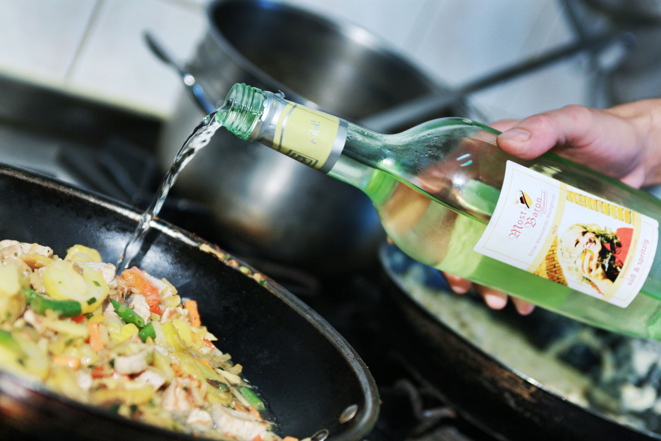 Eine Hand gießt Most aus einer Flasche in eine Pfanne mit Gemüse.