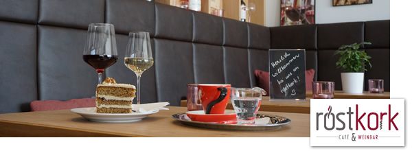 Innenansicht eines Cafés mit Weingläsern, Kuchen und einer Tafel auf einem Tisch.