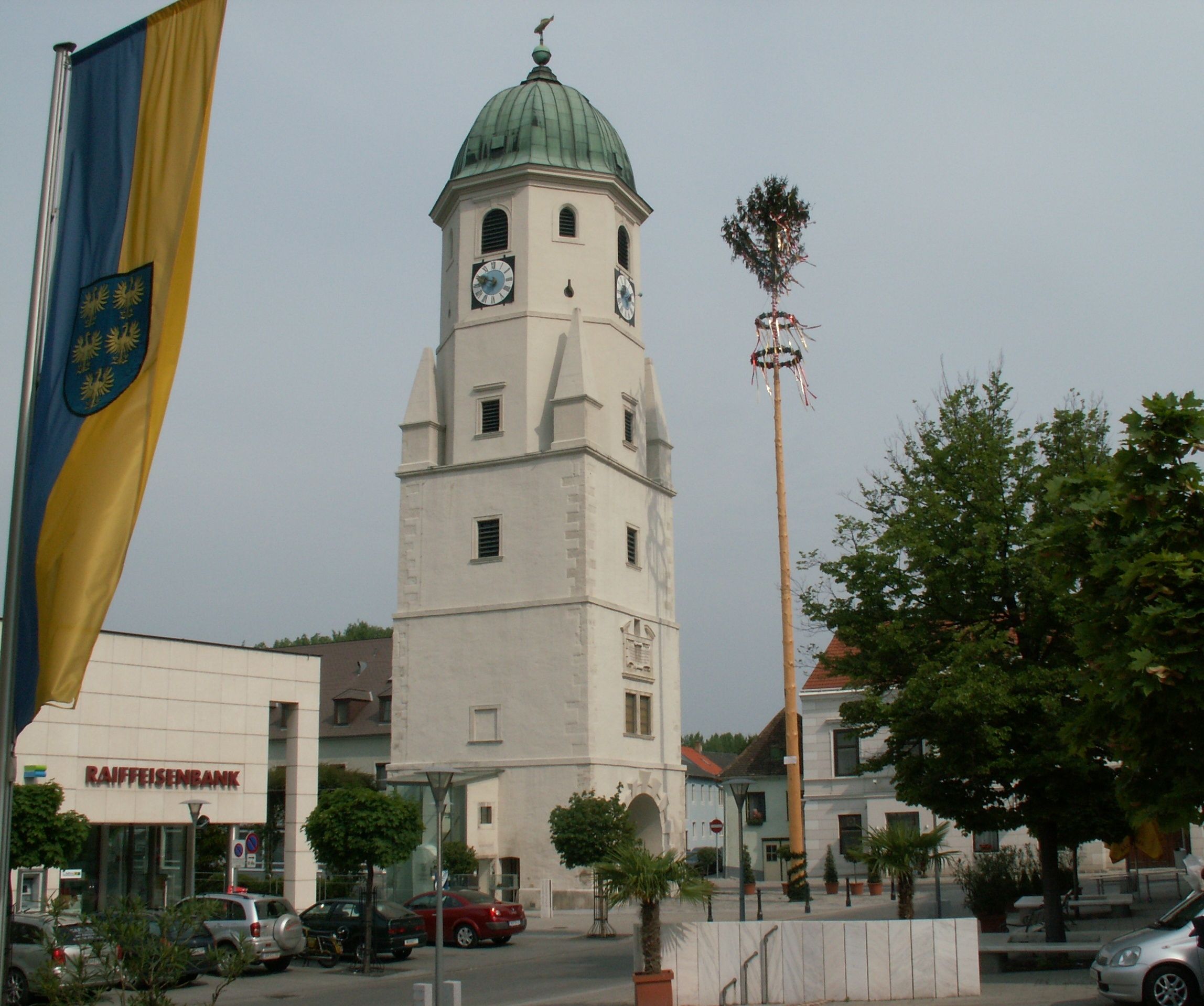 Stadtturm in Fischamend mit Maibaum und Flagge im Vordergrund.