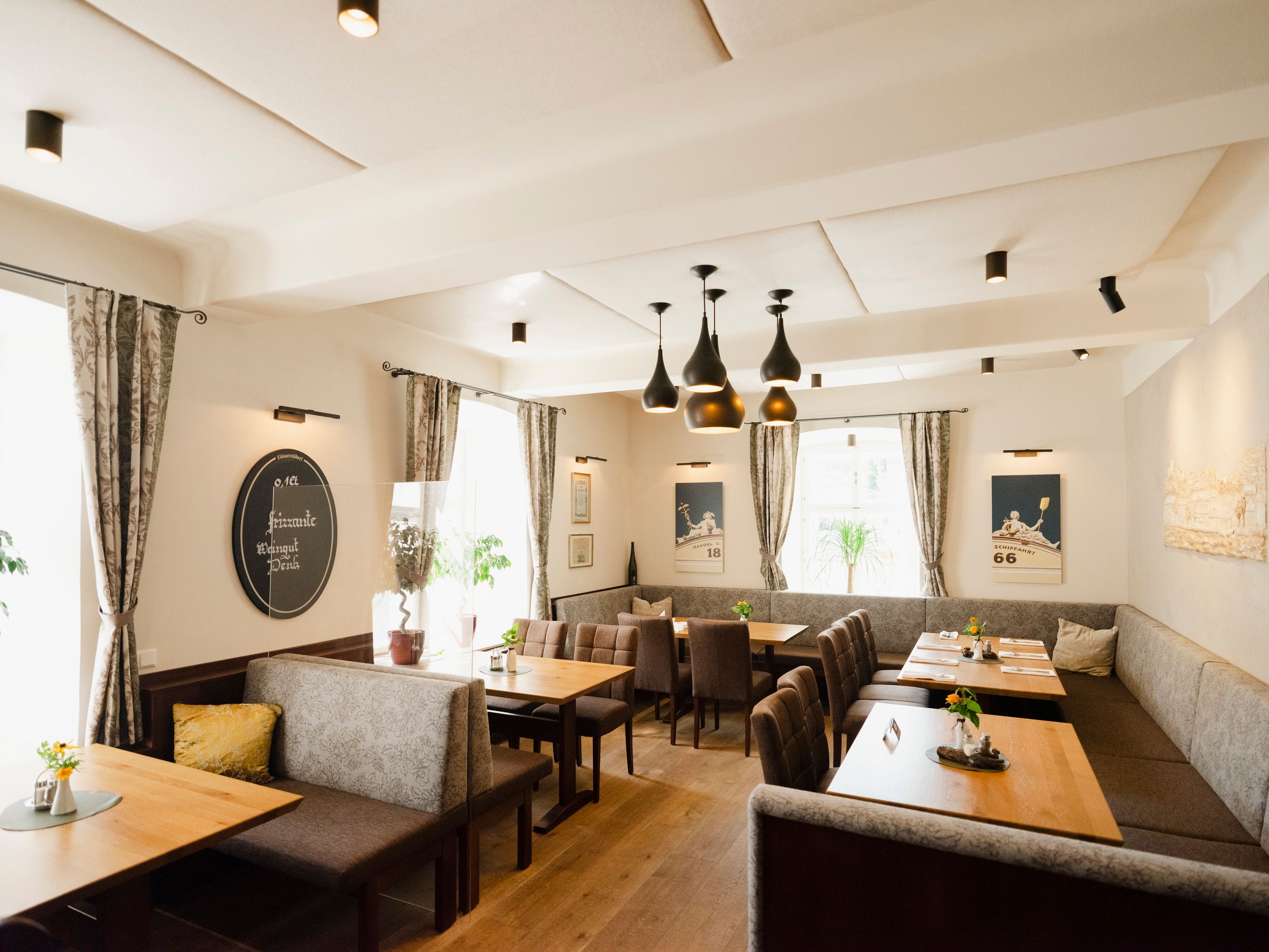 Modernes Restaurant mit Holztischen, grauen Polsterbänken und stilvollen Lampen.