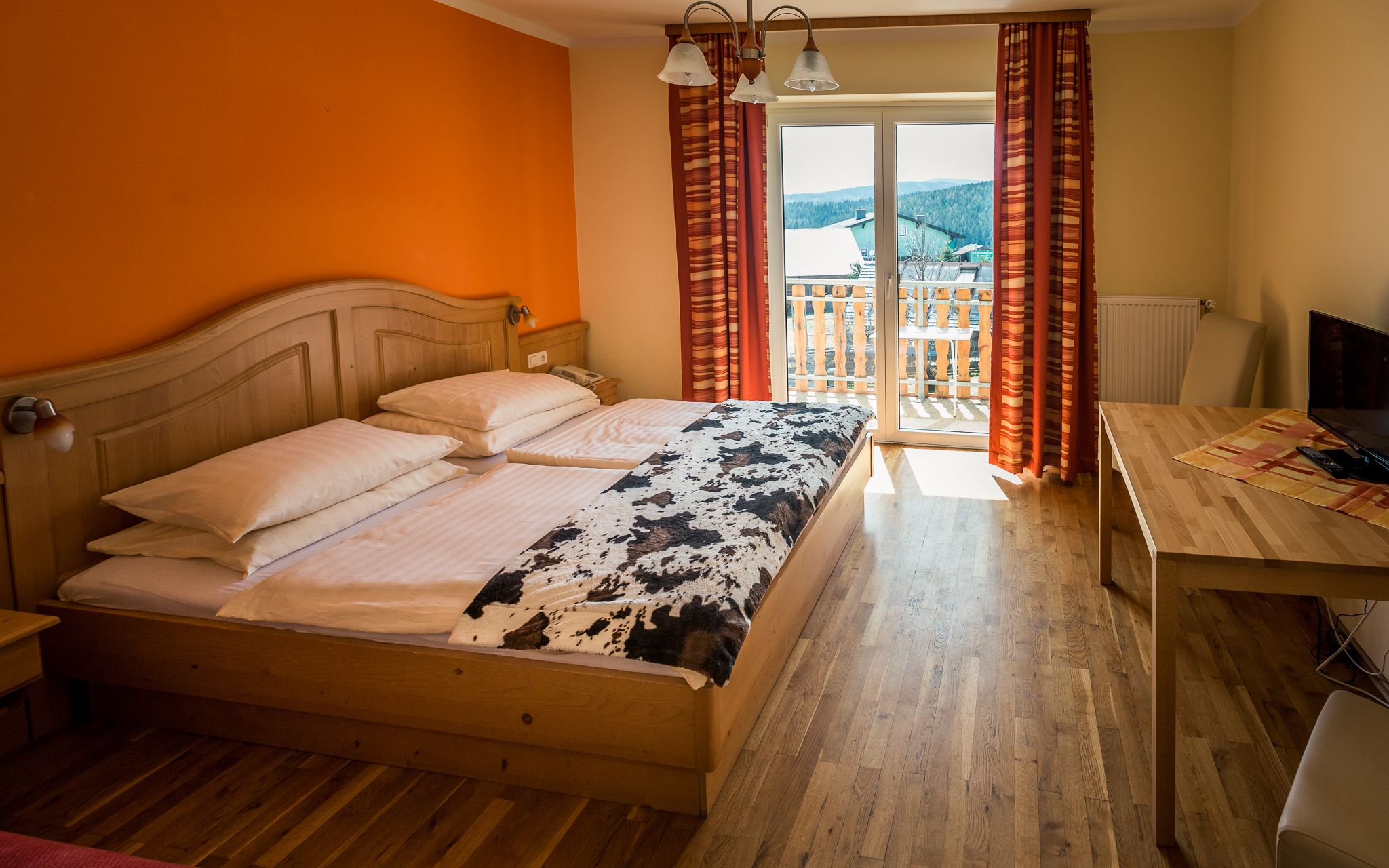 Gemütliches Hotelzimmer mit Doppelbett, Holzmöbeln und Balkon mit Ausblick.