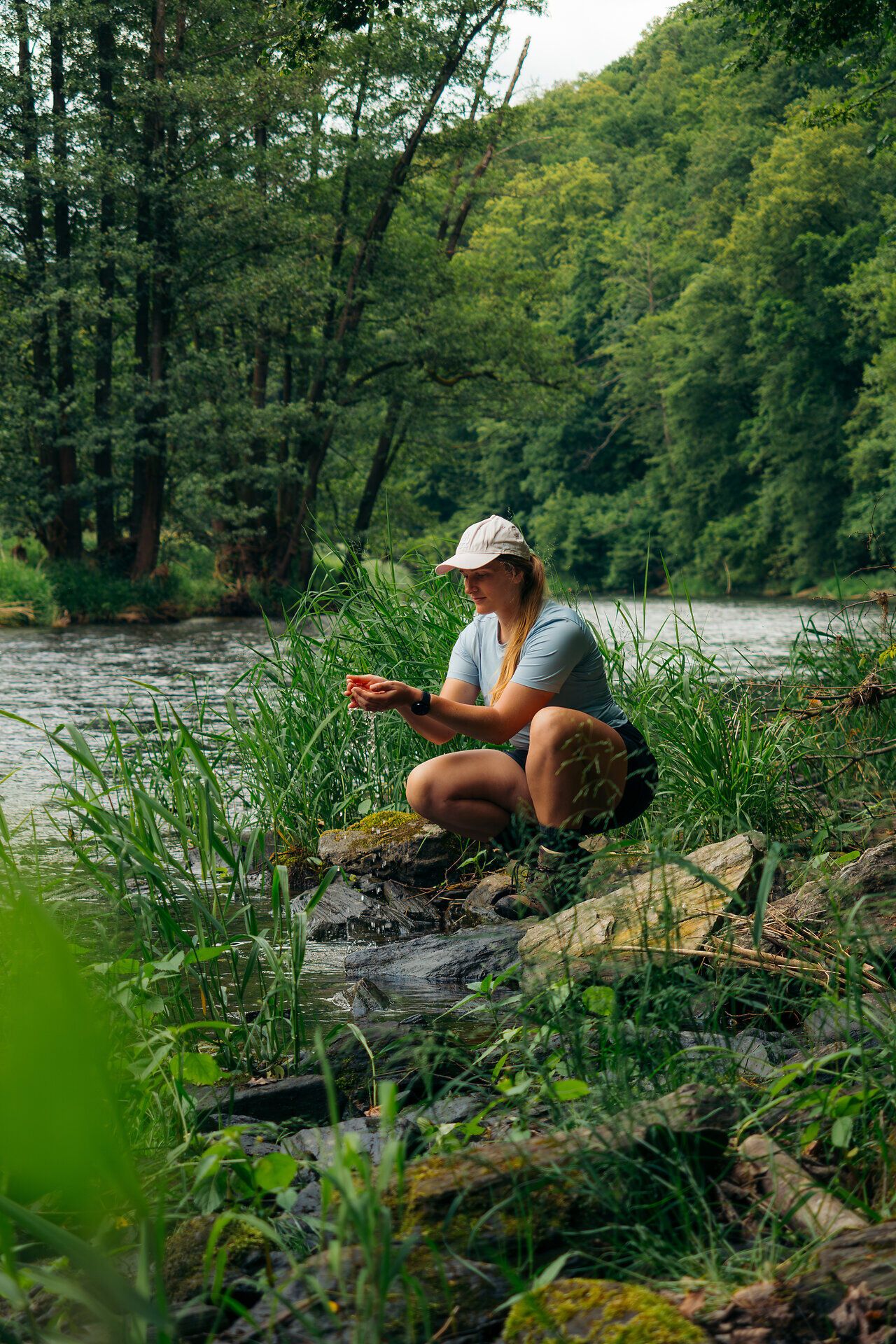Eine Frau kniet am Ufer der Thaya im Nationalpark Thayatal, umgeben von dichter Vegetation und reichem Grün.