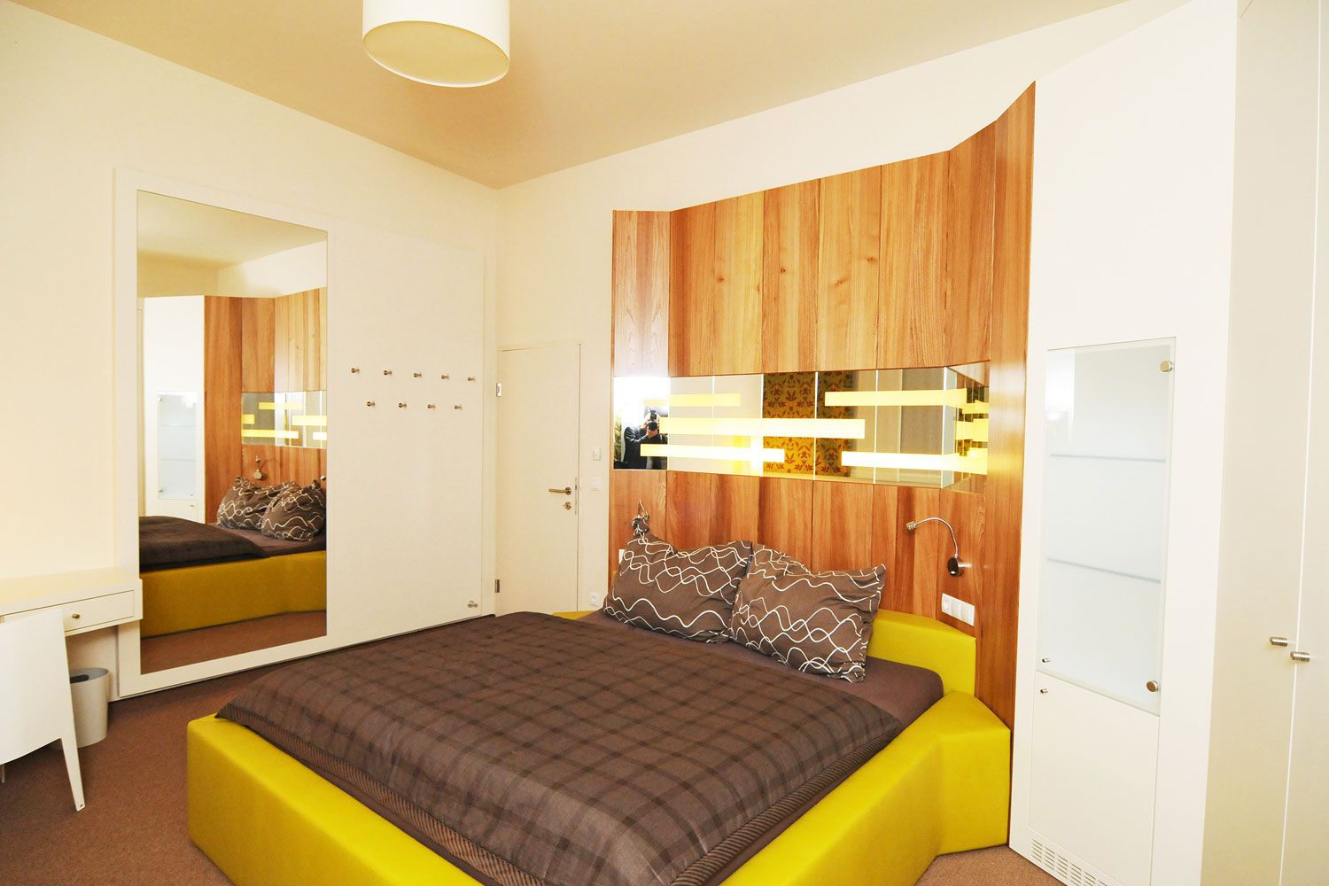 Modern eingerichtetes Schlafzimmer mit gelbem Bett und Holzverkleidung an der Wand.