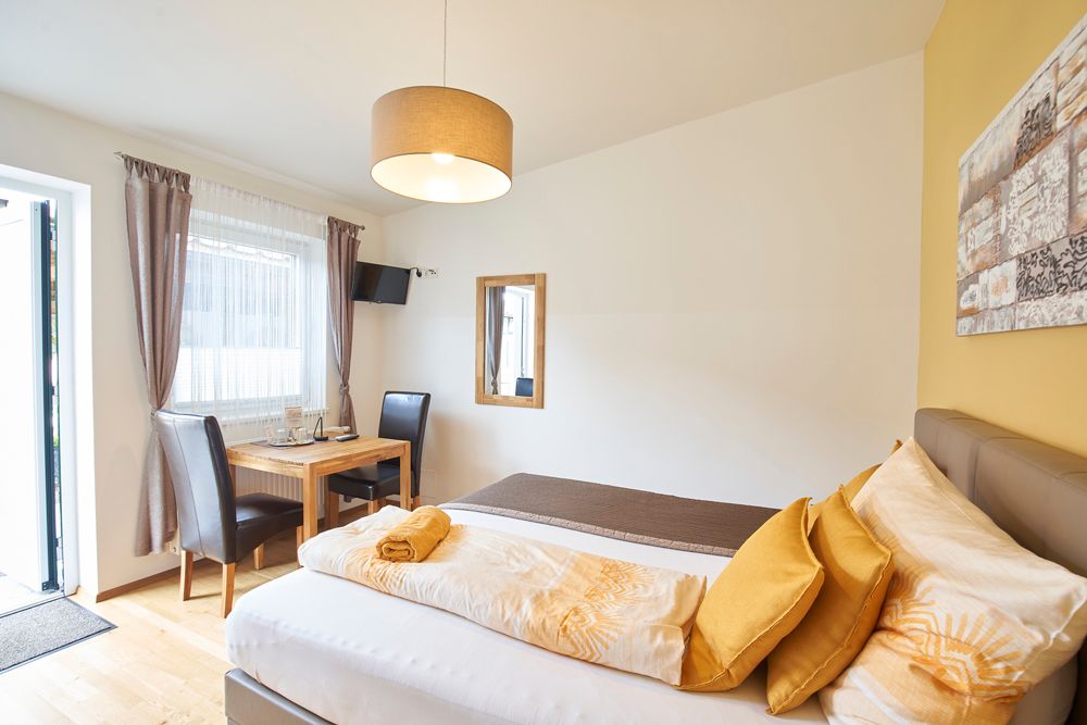 Helles Gästezimmer mit Bett, Tisch, Stühlen und Fernseher.