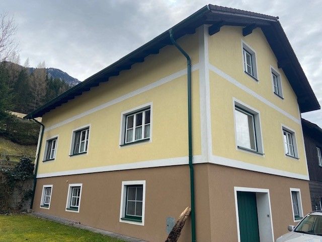 Zweistöckiges gelb-braunes Haus mit weißen Fensterrahmen und grünem Fallrohr.