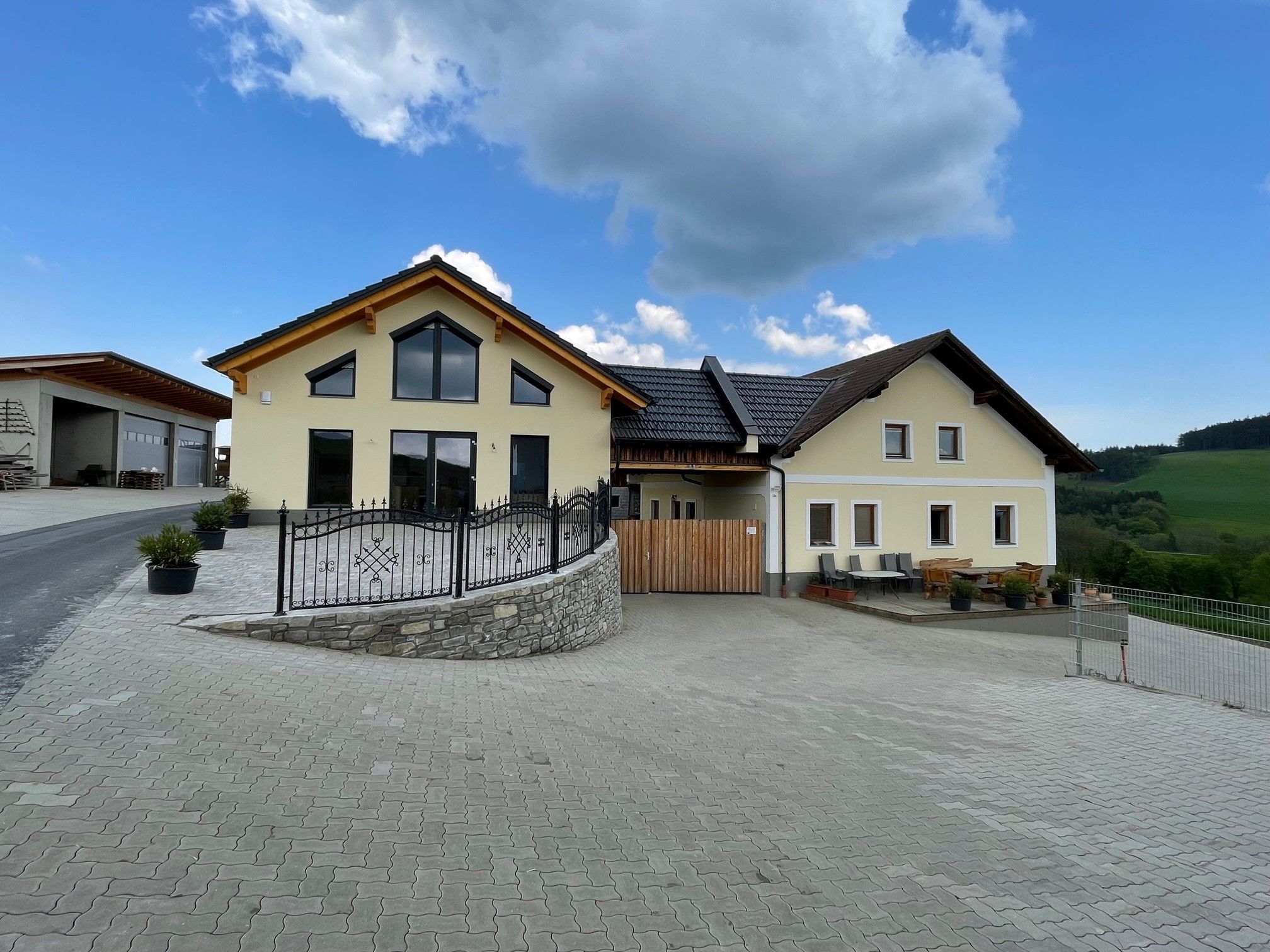 Gelbes Haus mit großen Fenstern auf gepflasterter Fläche unter blauen Himmel.