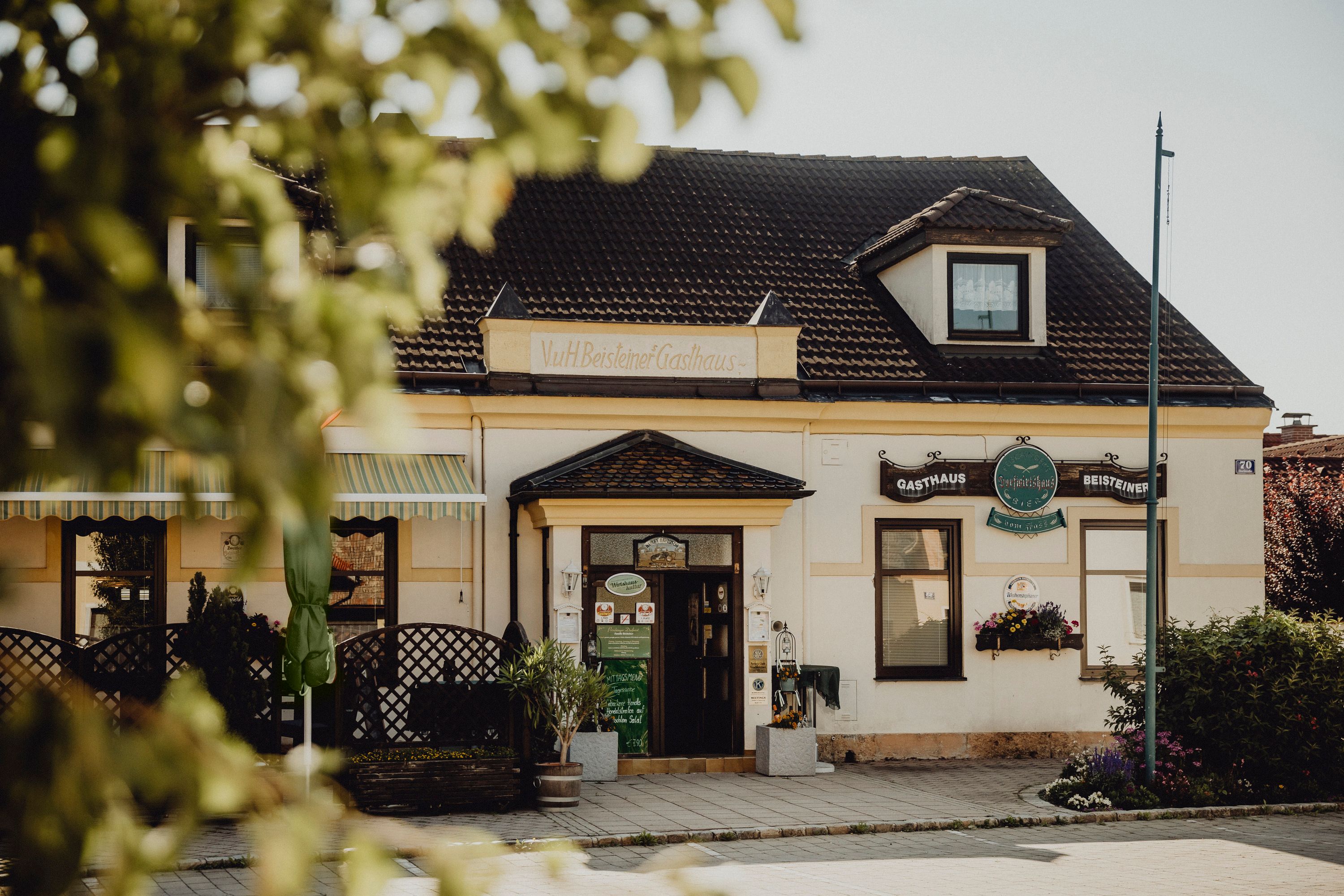 Traditionelles Gasthaus mit Schildern und Pflanzen im Vordergrund.