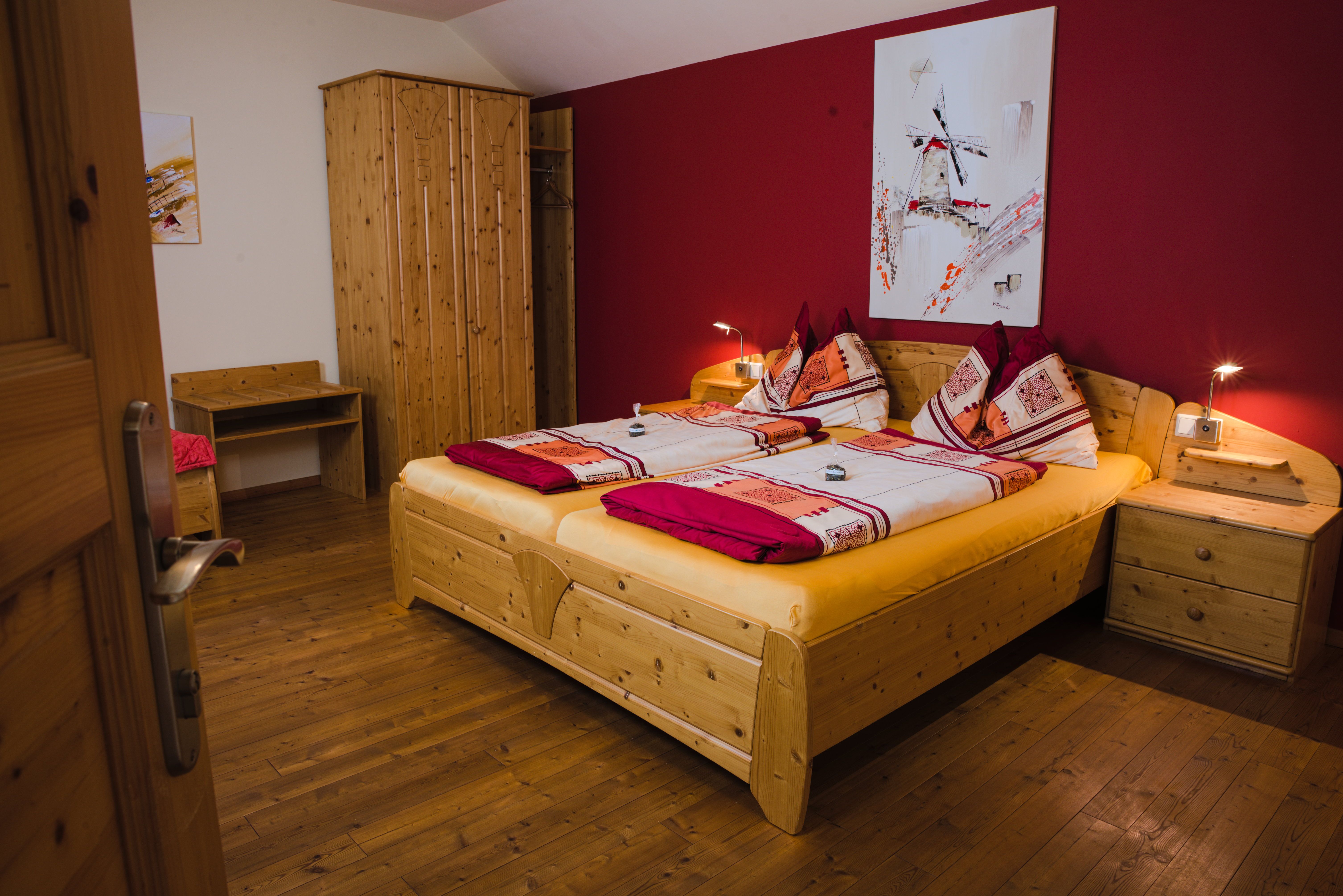 Gemütliches Gästezimmer mit Doppelbett, Holzmöbeln und roter Wand.