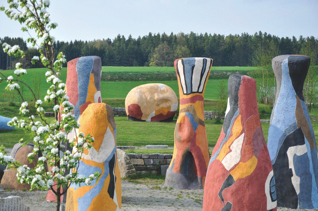 Bunte Skulpturen in einer grünen Landschaft mit Bäumen im Hintergrund.