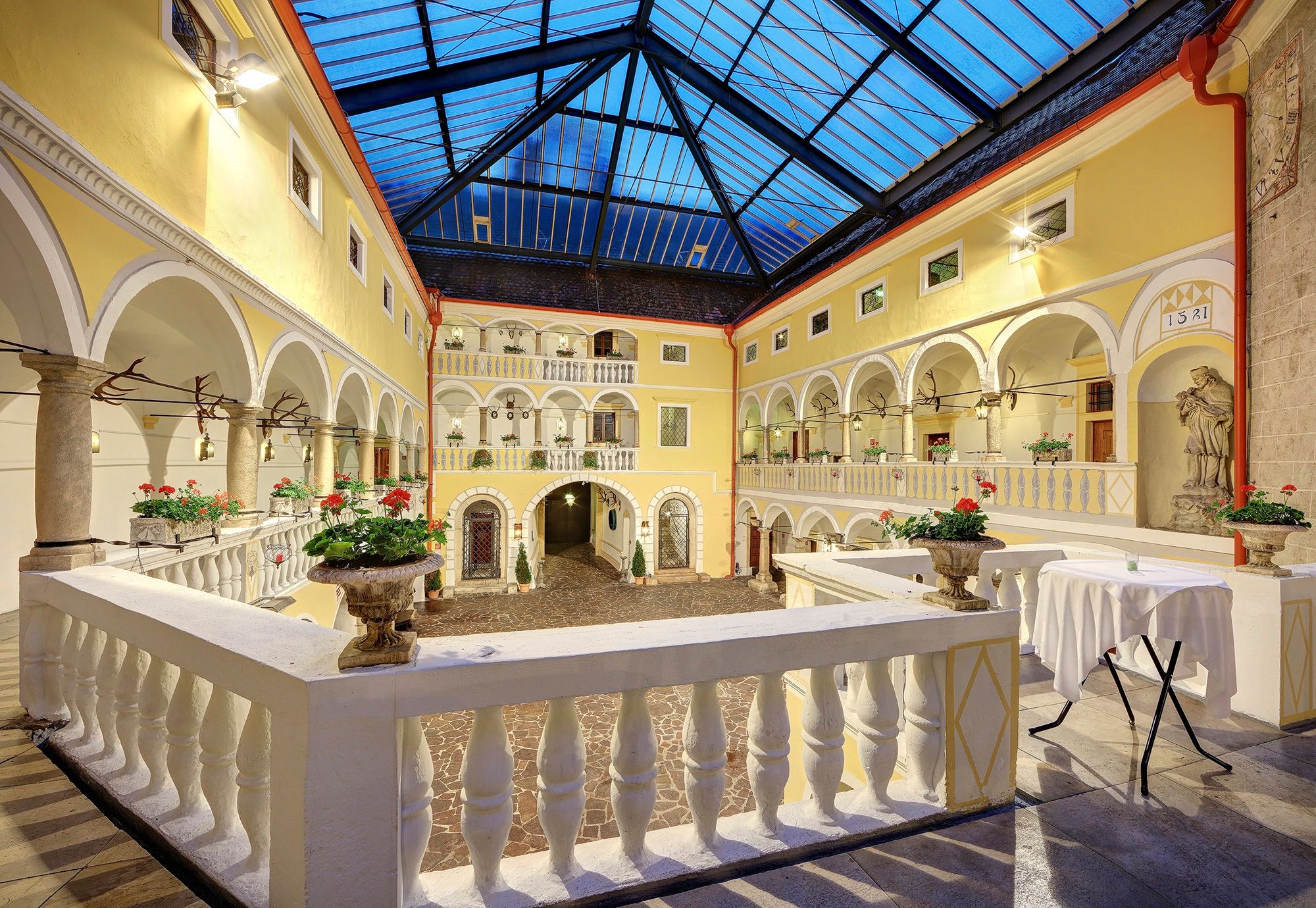 Innenhof mit Arkaden, gelben Fassaden, Glasdach und Blumenarrangements im H_WeikersdorfArkadenh_web.