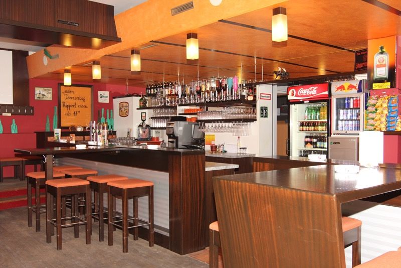 Innenansicht einer Bar mit Holzmöbeln, Barhockern und Getränken.