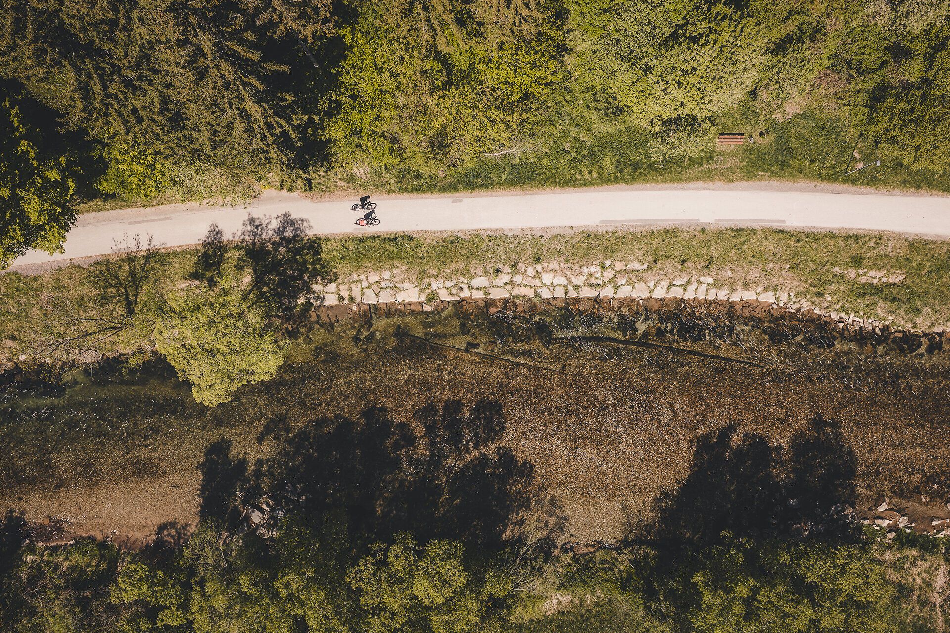 Zwei Radfahrerinnen fahren entlang des Radwegs neben einem Fluss.