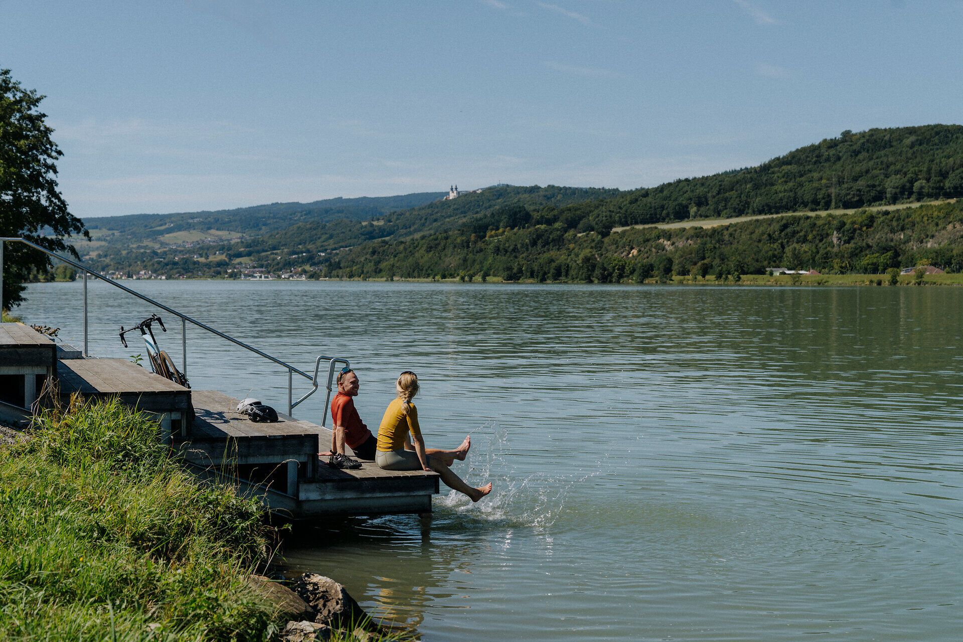 2 Radfahrer machen Pause beim Zehenbad an der Donau in Pöchlarn mit Blick auf die Donau und den Nibelungengau