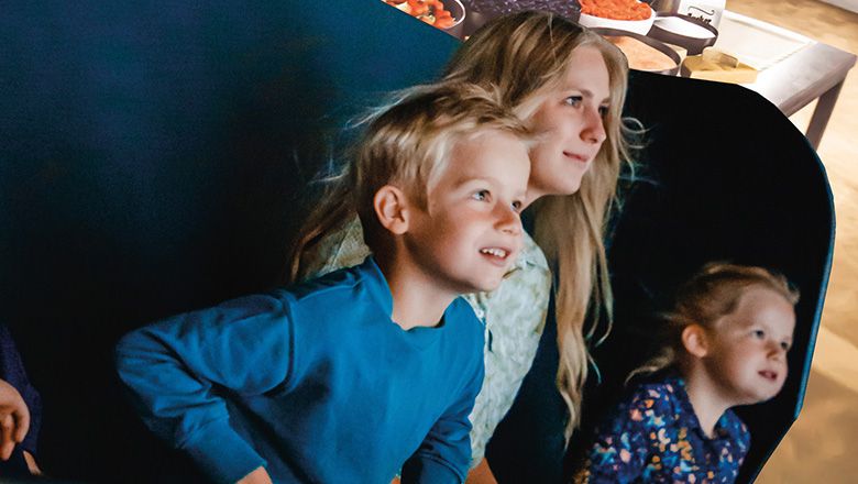 Zwei Kinder und eine Frau sitzen in einem Waggon im Flying-Theater und schauen gebannt nach vorne.