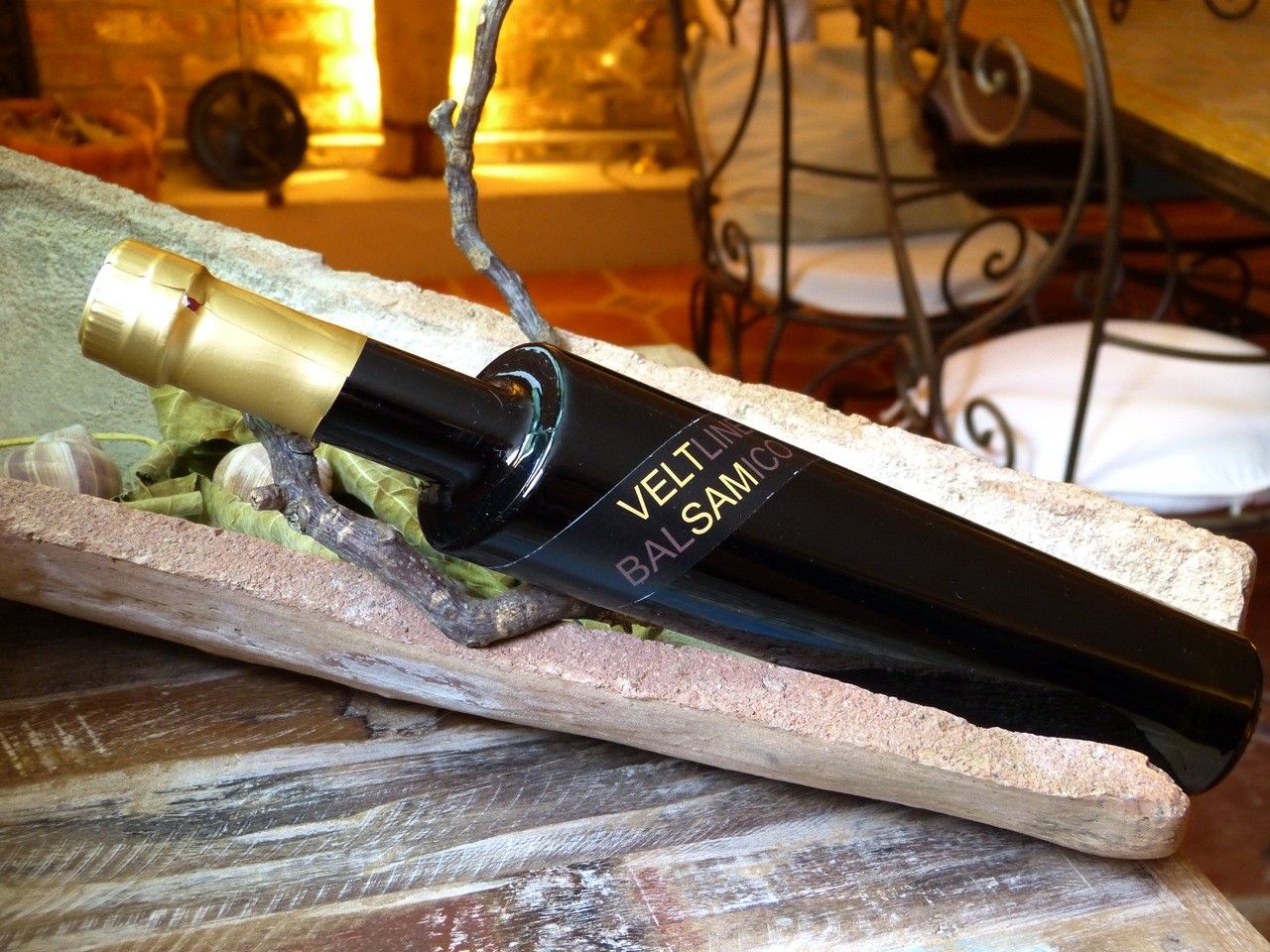 Eine schwarze Essigflasche mit goldener Kappe liegt in einer rustikalen Holzschale.