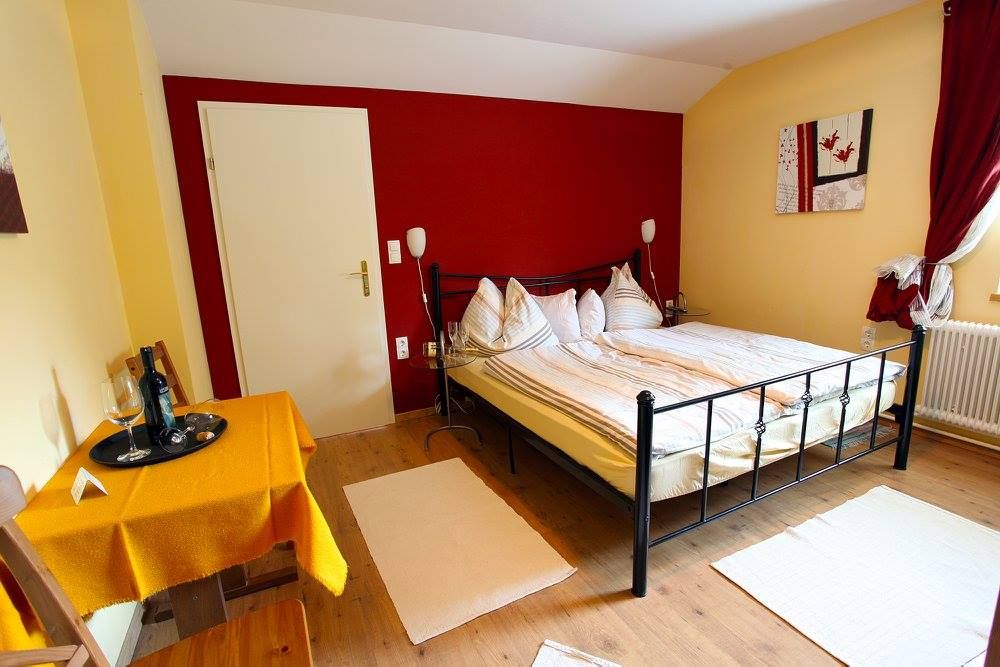 Gemütliches Schlafzimmer mit Doppelbett, Tisch und Stühlen, gelben Wänden und rotem Vorhang.