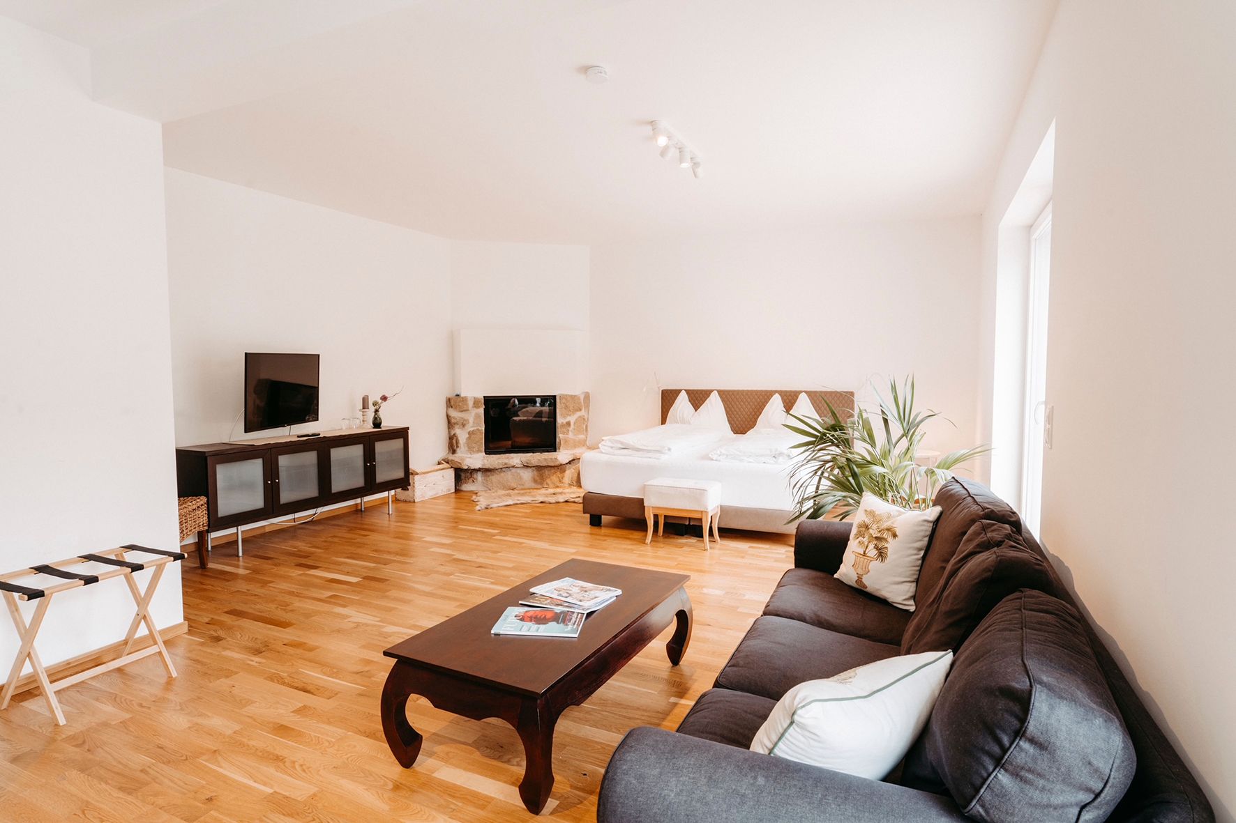 Helles Zimmer mit Sofa, Couchtisch, Fernseher, Kamin und Doppelbett.