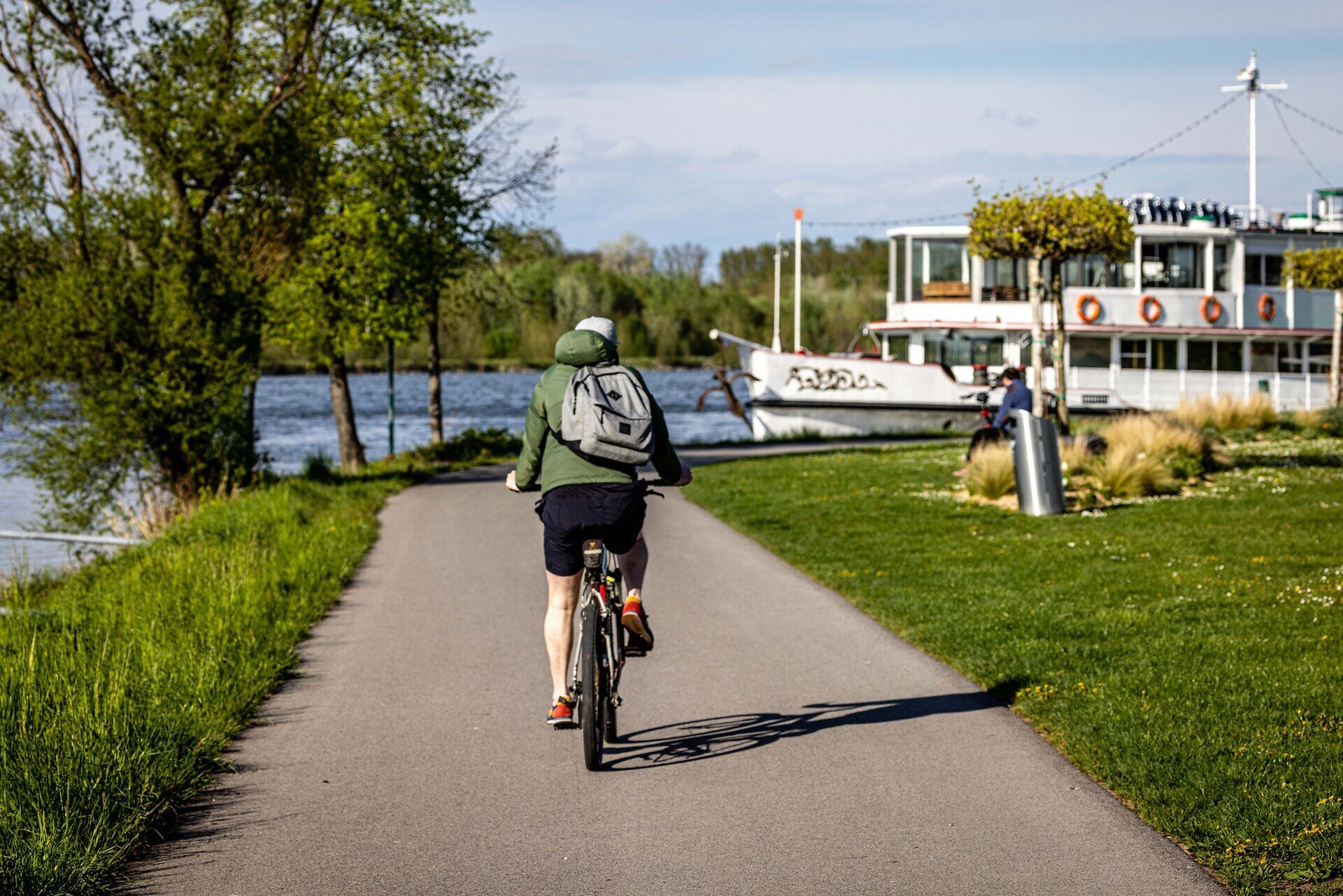 Fahrradfahrer auf dem Donauradweg in Tulln mit Blick auf ein großes Schiff