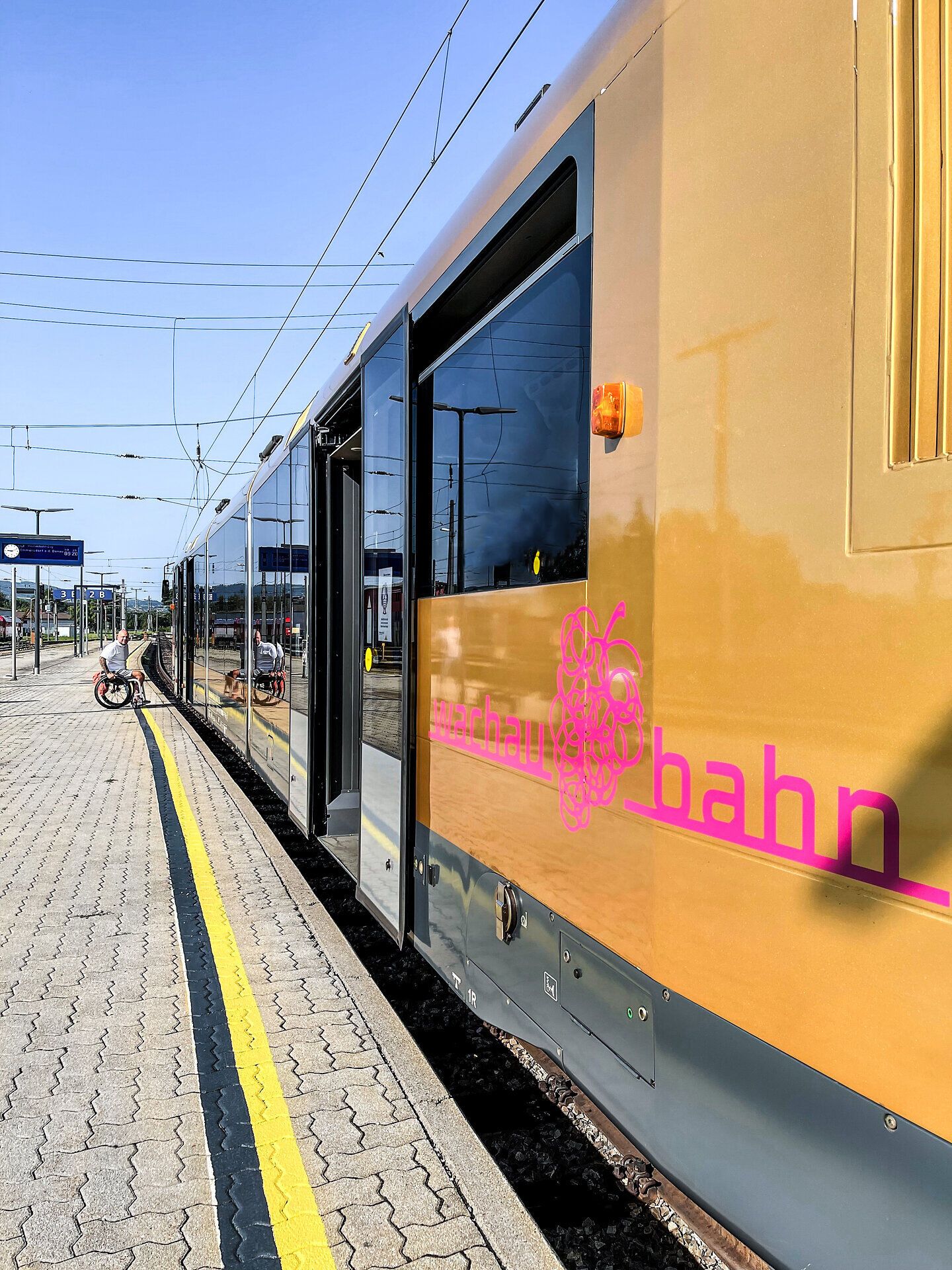 Die Wachaubahn schlängelt sich durch die malerische Landschaft, während die sanften Hügel und die glitzernde Donau im Hintergrund eine idyllische Kulisse bieten. Ein perfekter Ort, um die Schönheit der Region zu entdecken und die frische Luft der Natur zu genießen.