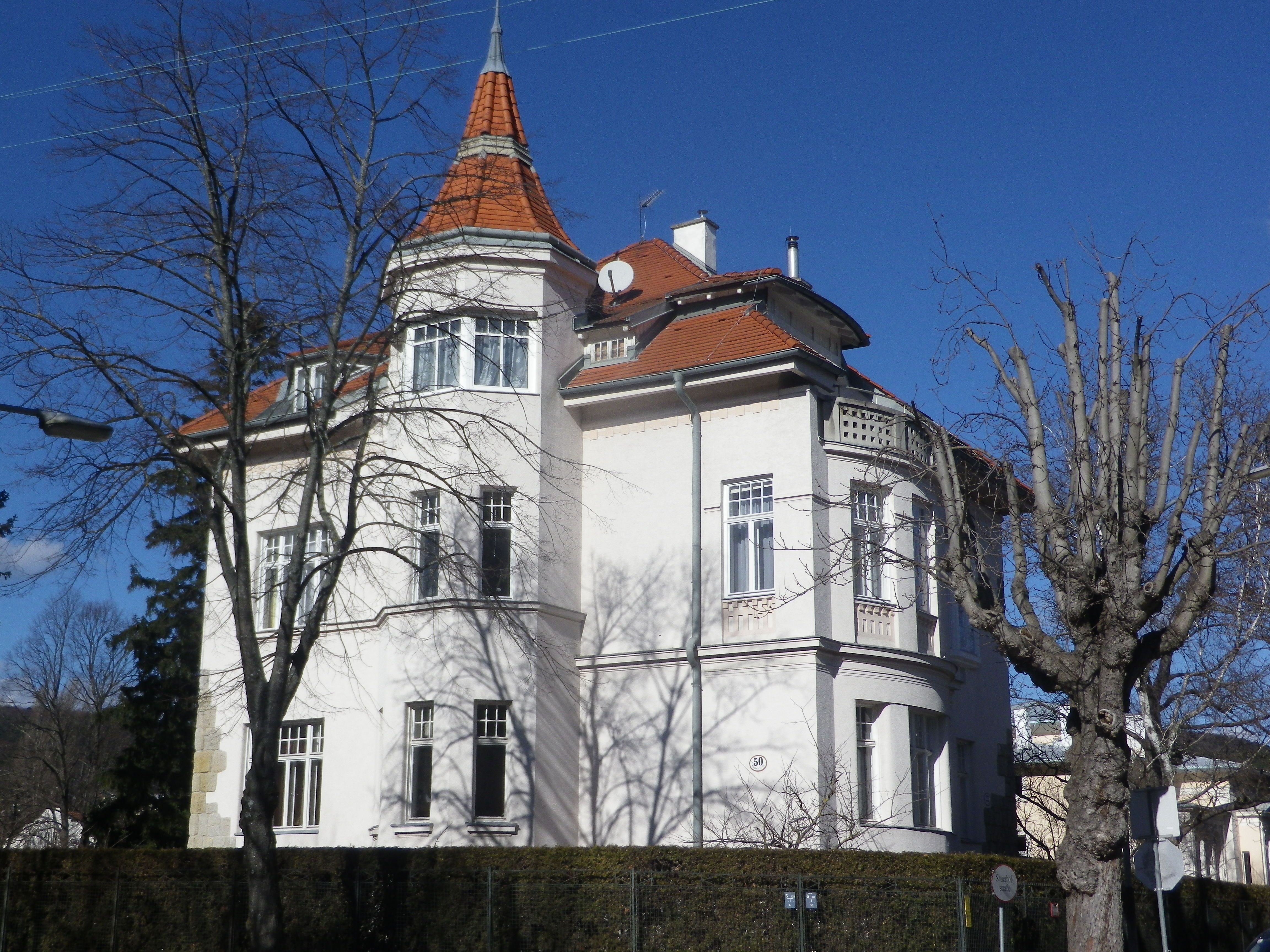 Großes weißes Haus mit rotem Dach und Turm, umgeben von kahlen Bäumen.