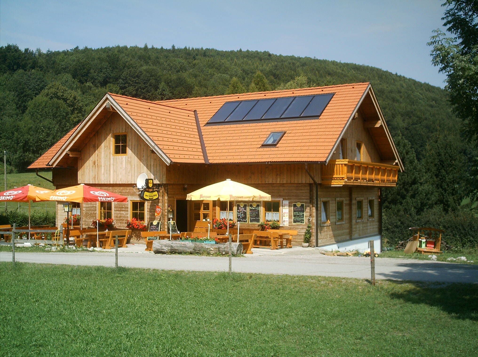 Ein traditionelles Gasthaus mit Holzwänden und roten Dachziegeln, umgeben von grüner Landschaft und Wald.