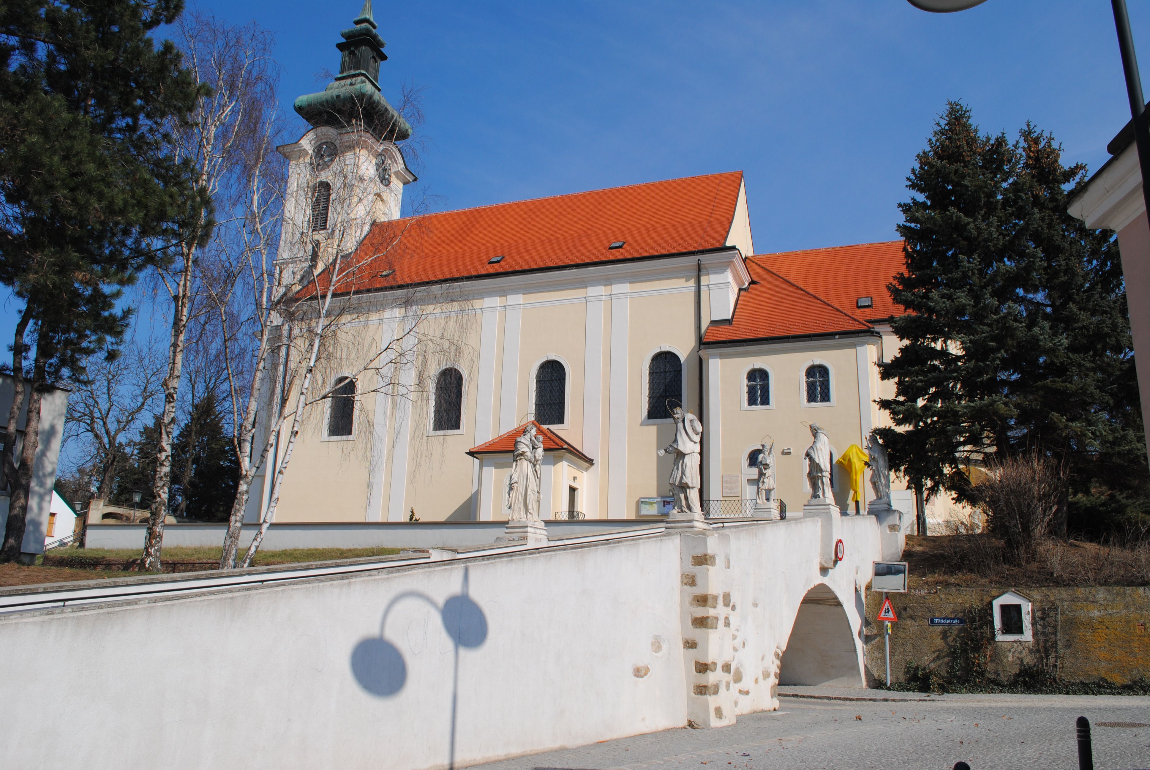 Pfarrkirche Wolkersdorf mit Statuen auf einer Brücke, blauer Himmel.