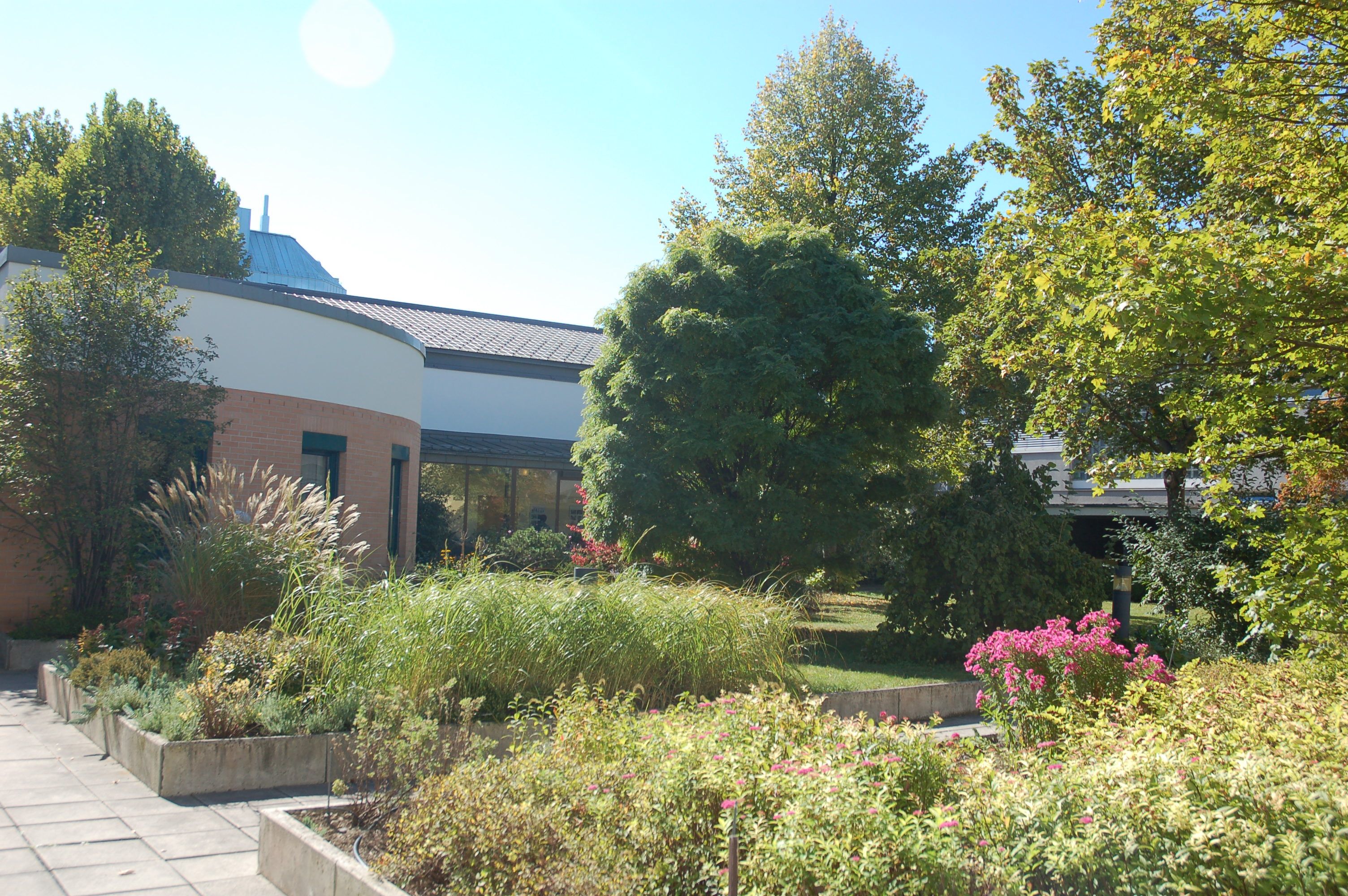 Garten des Bildungshauses St. Hippolyt mit Pflanzen und Bäumen vor einem modernen Gebäude.