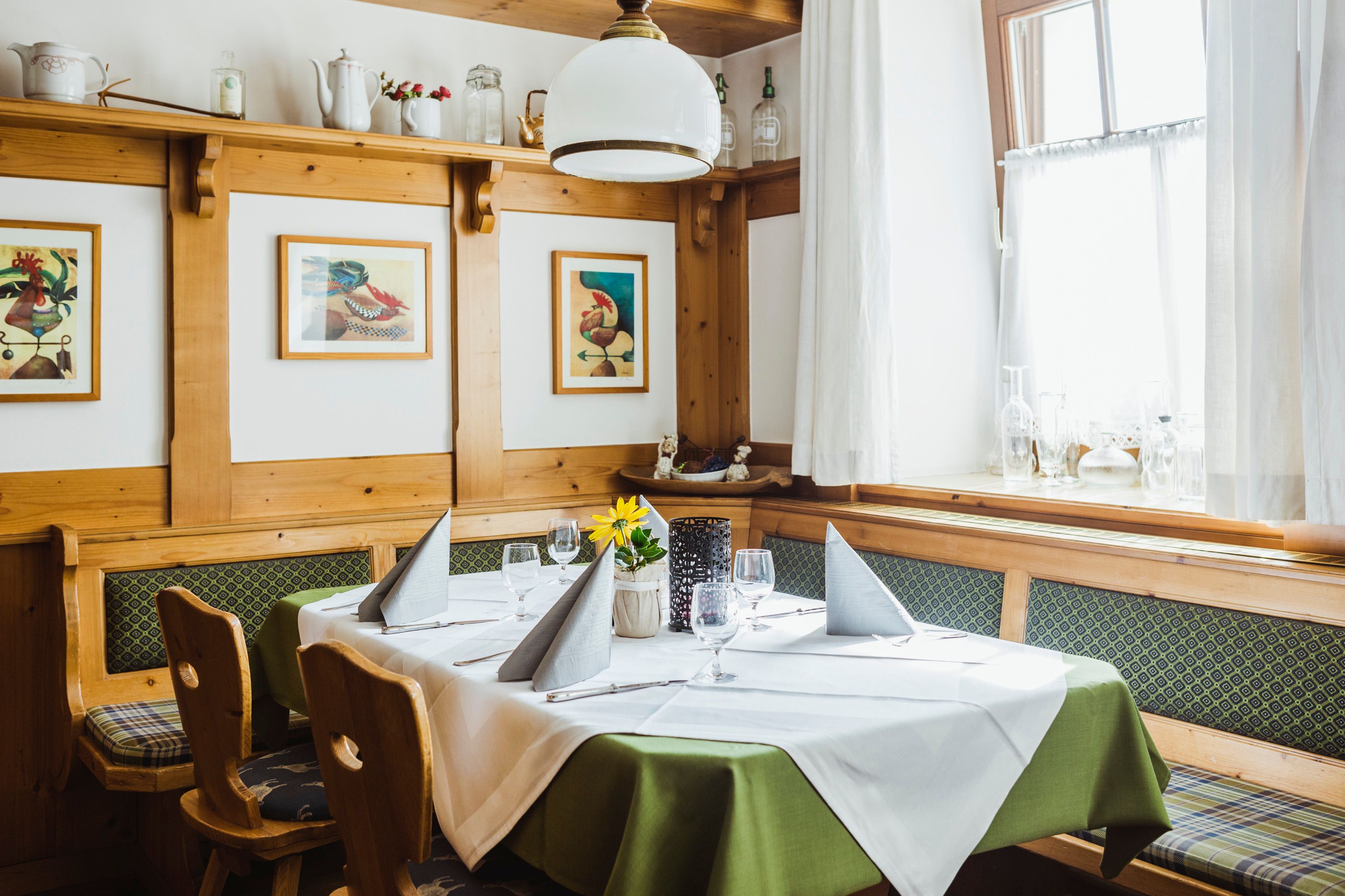 Gemütliche Stube mit Holzmöbeln, gedecktem Tisch und Bildern an der Wand.