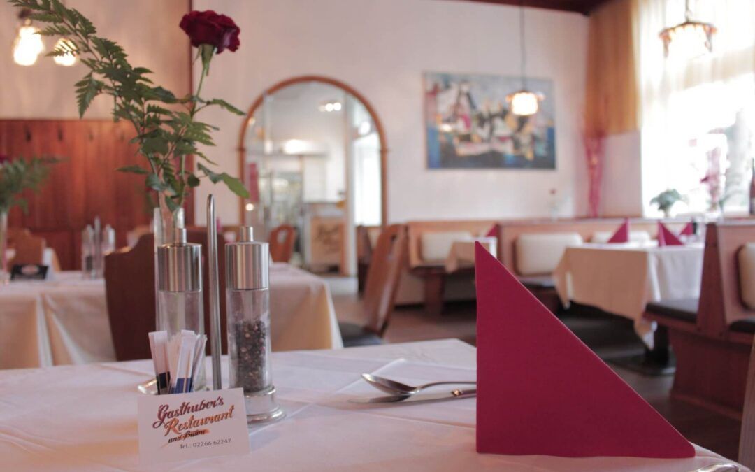 Innenansicht eines gemütlichen Restaurants mit gedeckten Tischen, roten Servietten und einer Rose in einer Vase.
