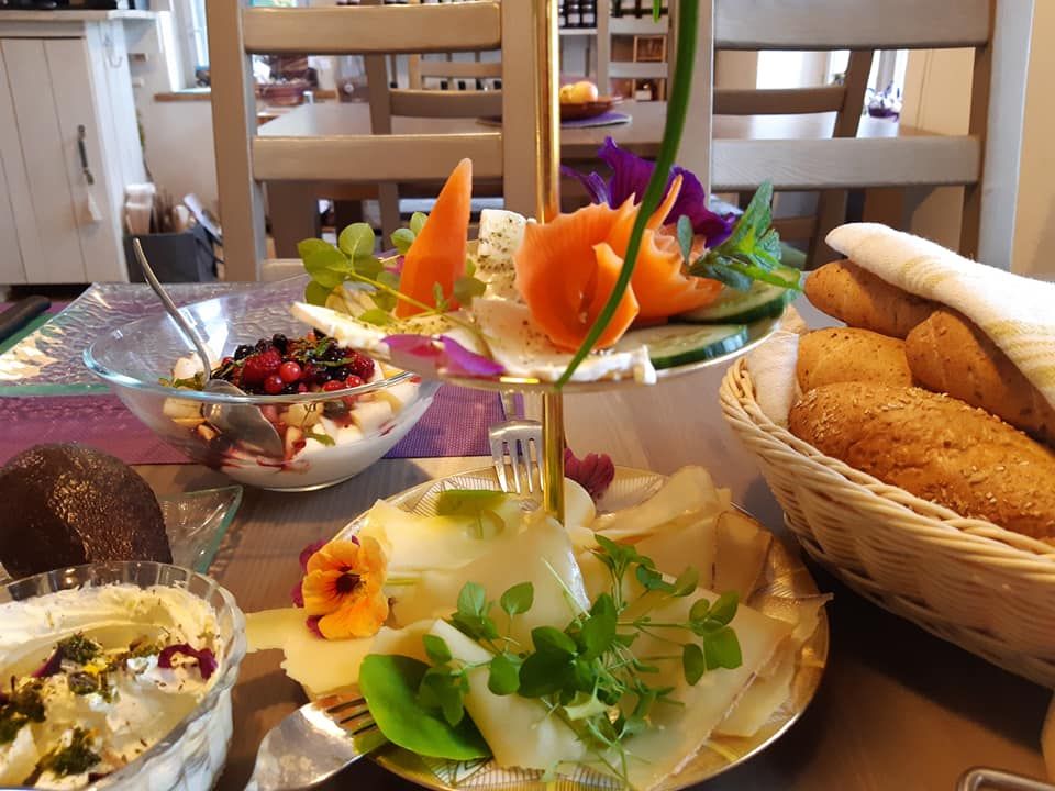 Ein gedeckter Frühstückstisch mit Brötchen, Käse, Joghurt mit Beeren und dekorativen Blumen.