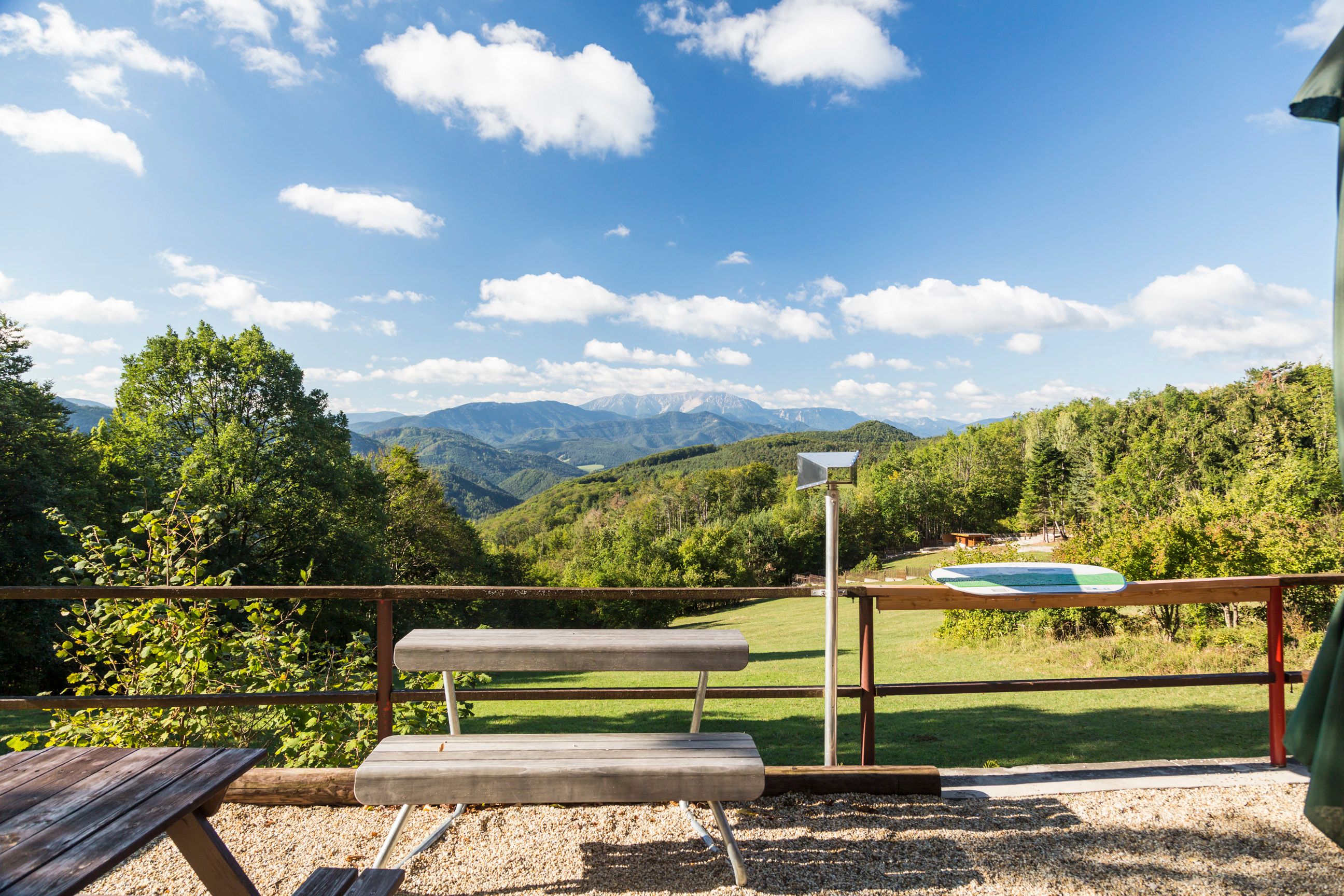 Aussicht vom Waxeneckhaus auf bewaldete Hügel und Berge unter blauem Himmel mit Wolken.