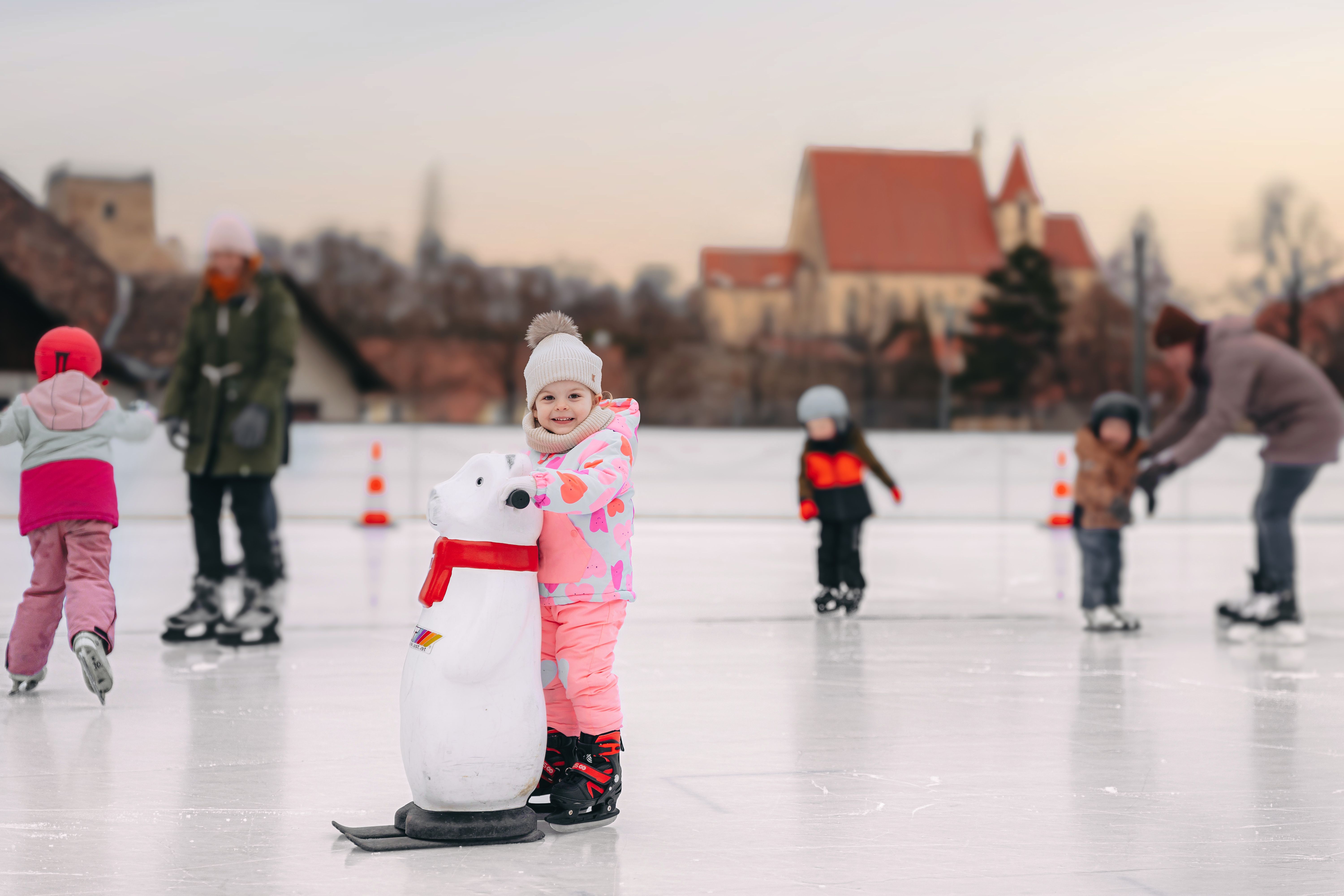 Kinder beim Eislaufen auf einem Platz mit einer Kirche im Hintergrund.