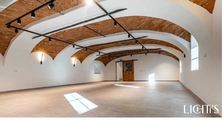 Leerer Veranstaltungsraum mit gewölbter Ziegeldecke und Holztür.