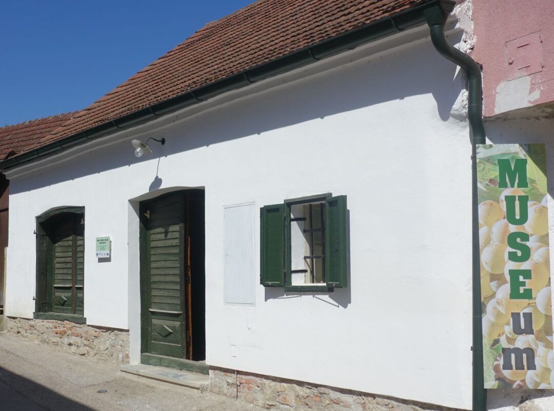 Weißes Gebäude mit grünem Fensterladen und Tür, Schild mit Aufschrift 'MUSEUM'.