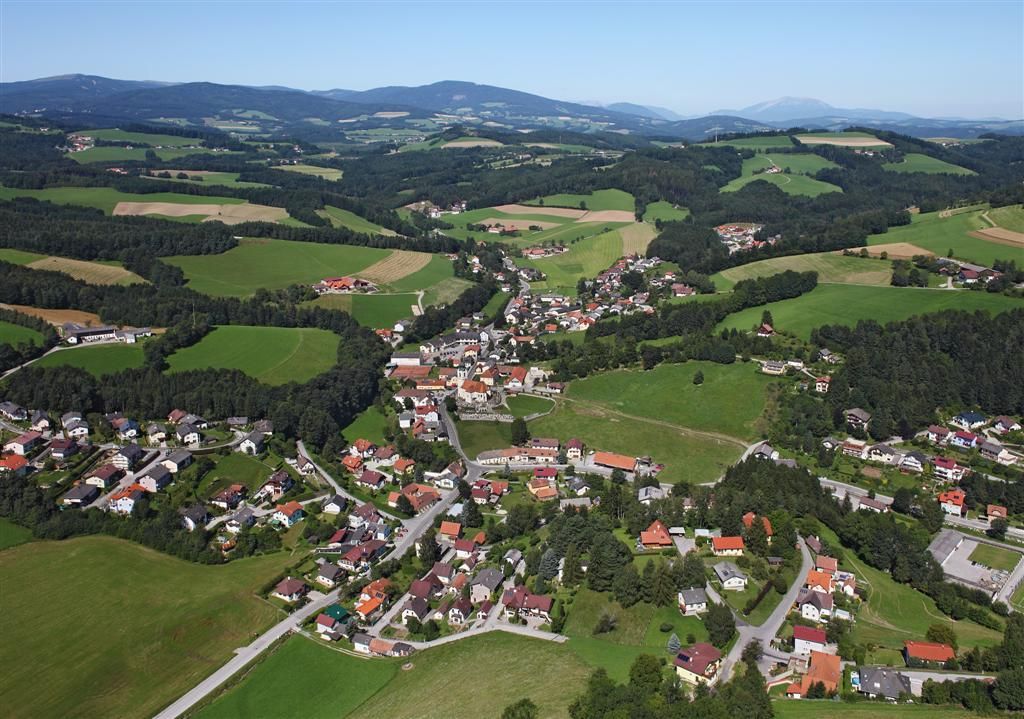 Luftaufnahme von Zöbern, einer ländlichen Gemeinde mit Häusern und Feldern, umgeben von Hügeln und Wäldern.