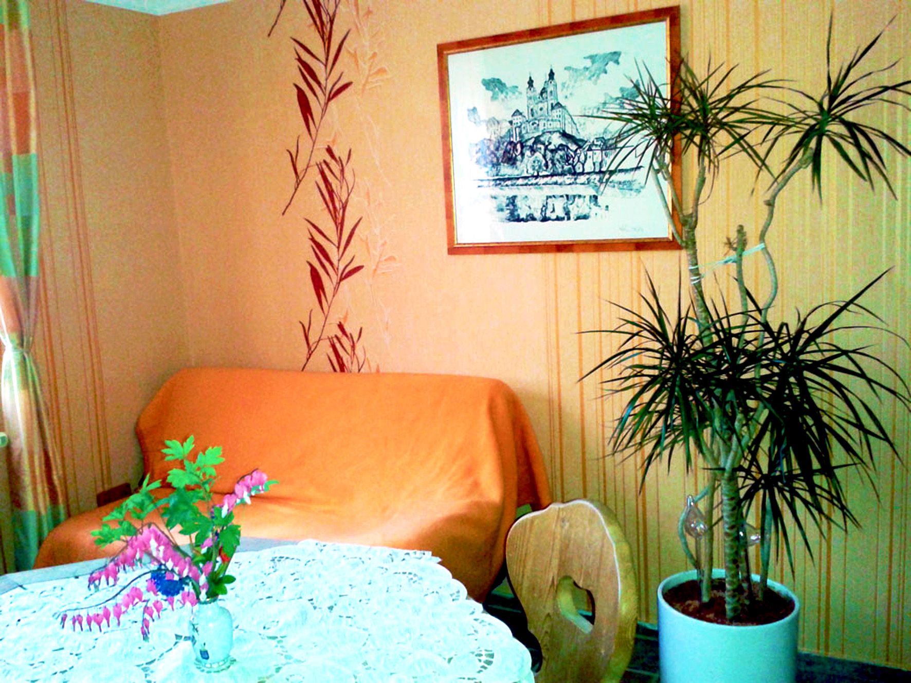 Gemütlicher Raum mit Sofa, Pflanze und Tisch mit Blumen.