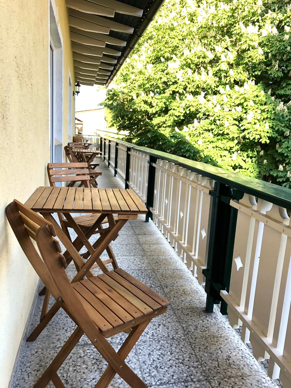 Holzbalkon mit Tisch und Stühlen, daneben grüne Bäume.