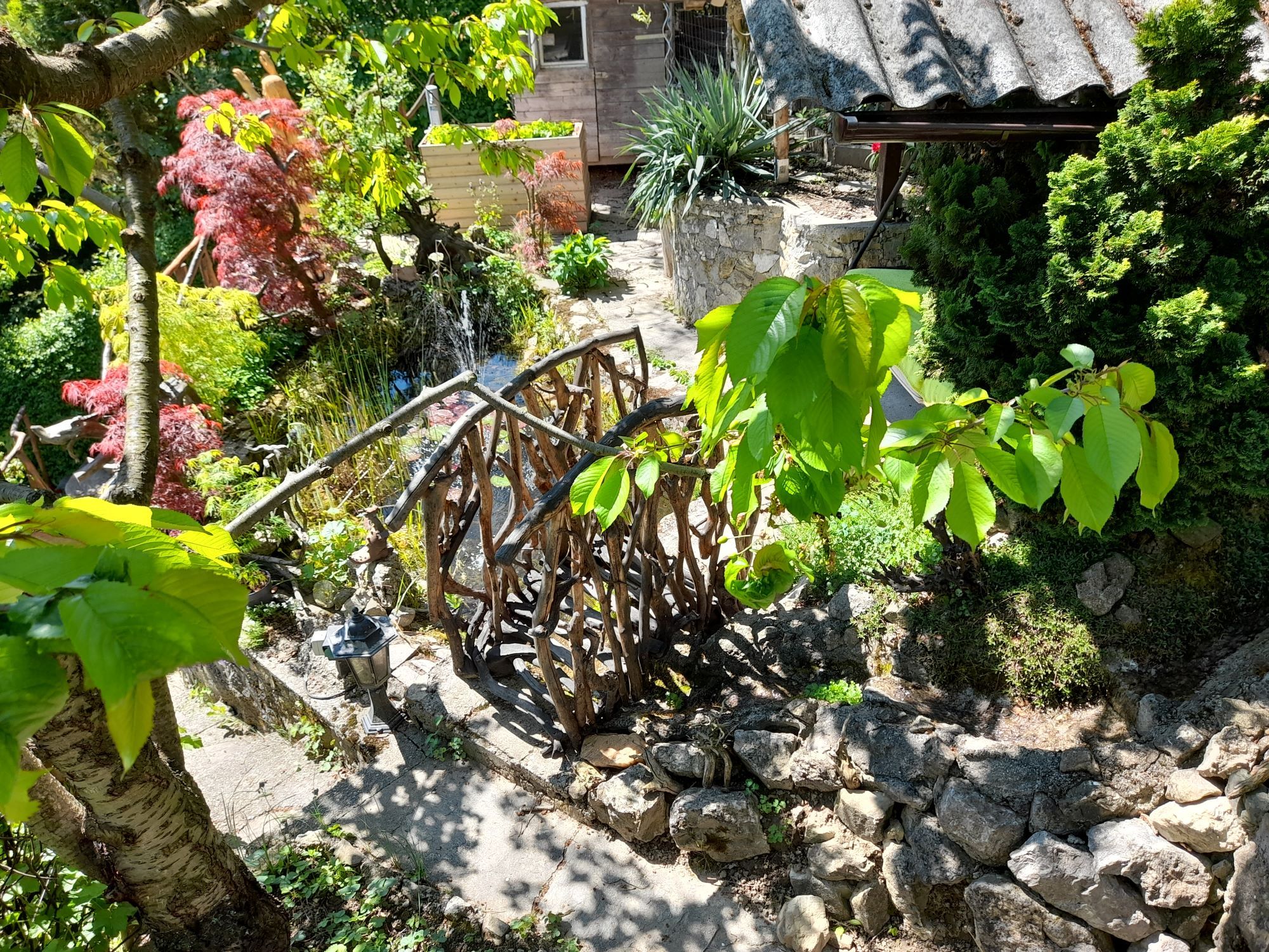 Garten mit Holzbrücke, Pflanzen und Steinen.