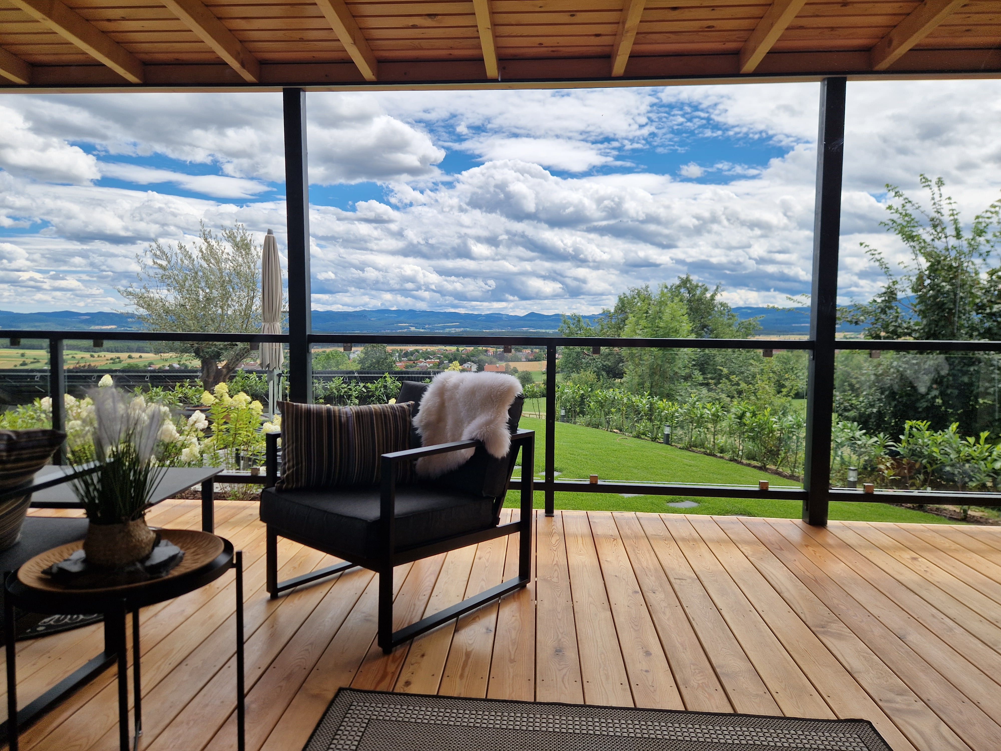 Terrasse mit Holzboden, modernen Möbeln und Blick auf eine grüne Landschaft und Berge.